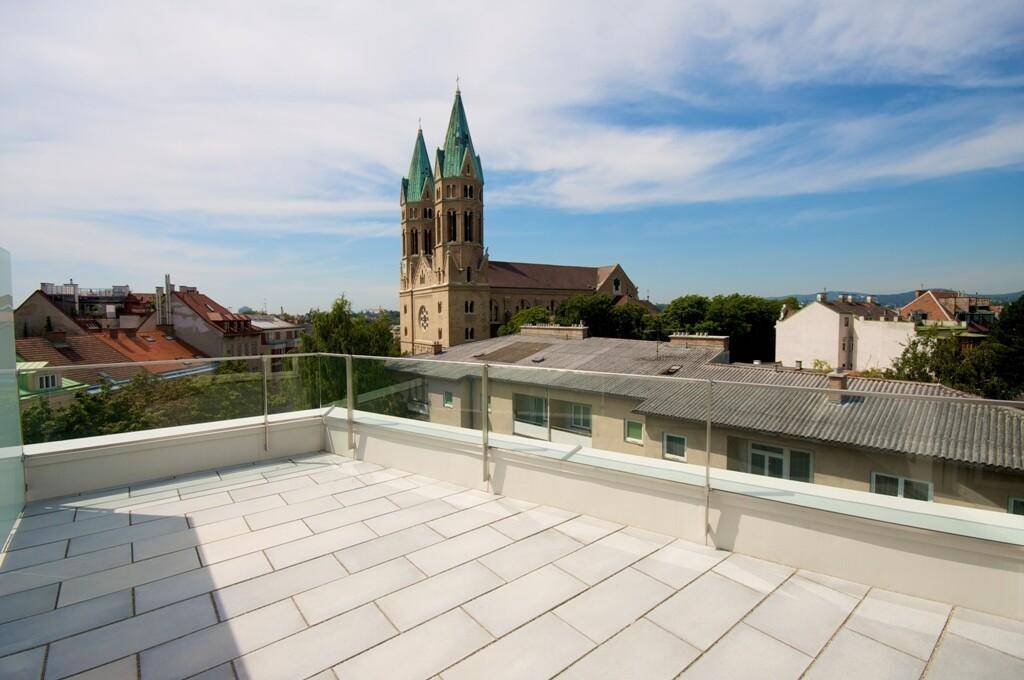 Geräumige Dachterrasse mit Glasgeländer und einem malerischen Blick auf die Stadt und eine historische Kirche.