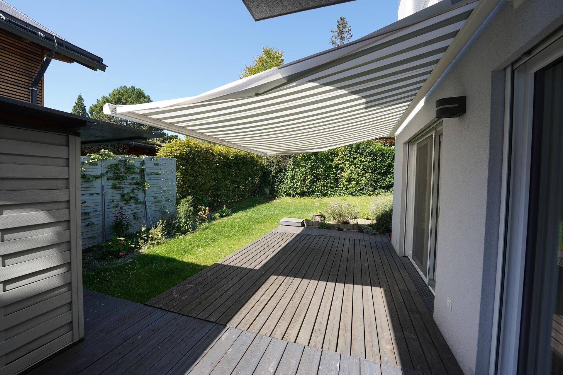 Geräumige Holzterrasse mit ausfahrbarer Markise und Zugang zum Garten, bietet Schatten und Komfort.