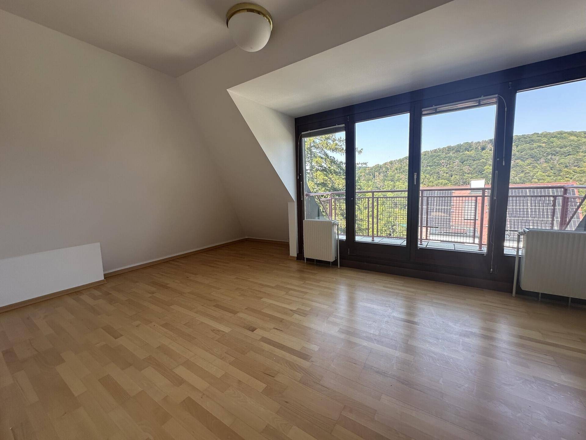 Helles Schlafzimmer im Dachgeschoss mit Holzboden und großen Fenstern mit Balkonzugang.