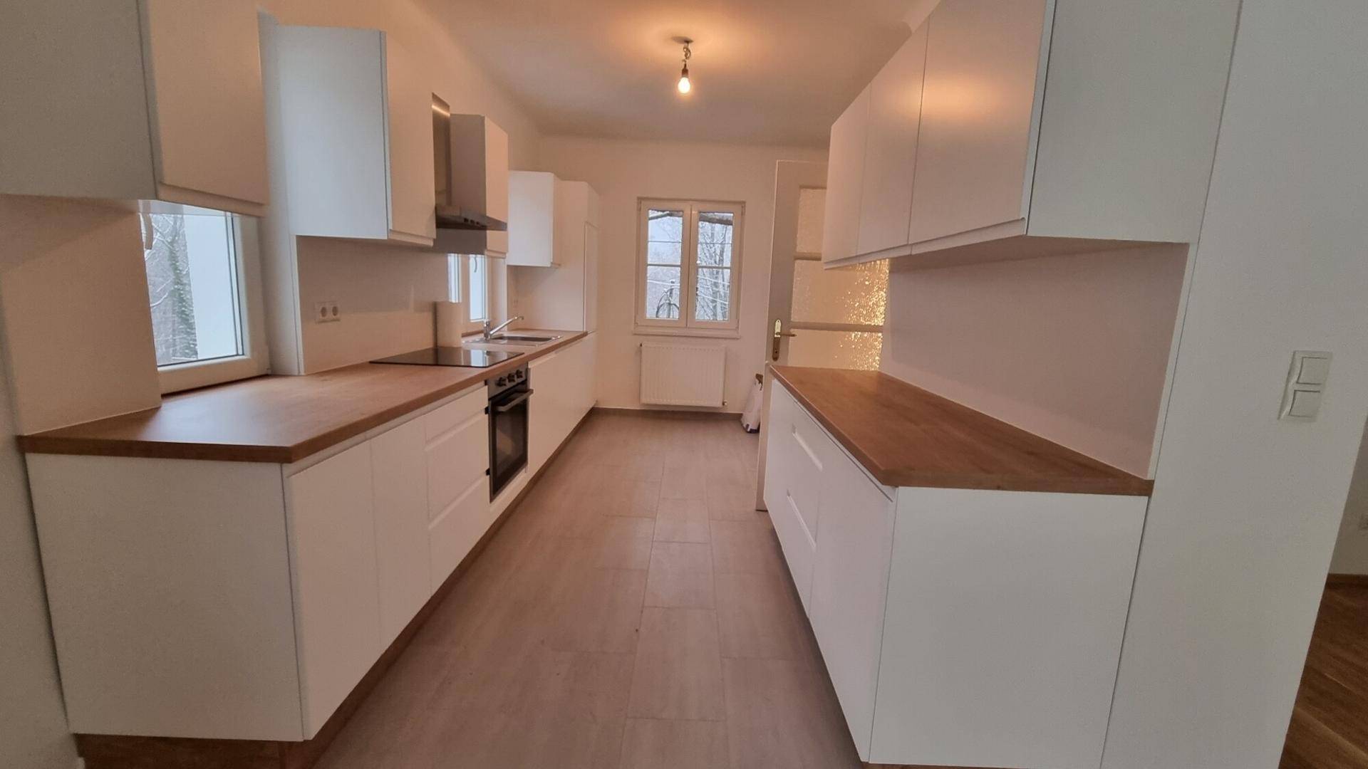Moderne Küche mit weißen Schränken, Holz-Arbeitsplatten und Fliesenboden.
