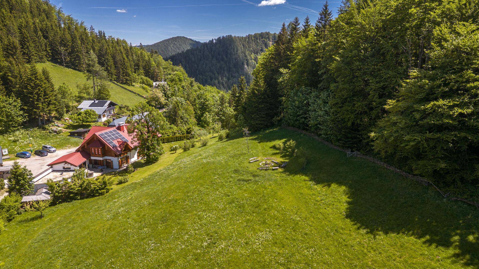 Luftaufnahme des Anwesens mit Chalet-Haus, weitläufigen Wiesen und umliegenden Wäldern.