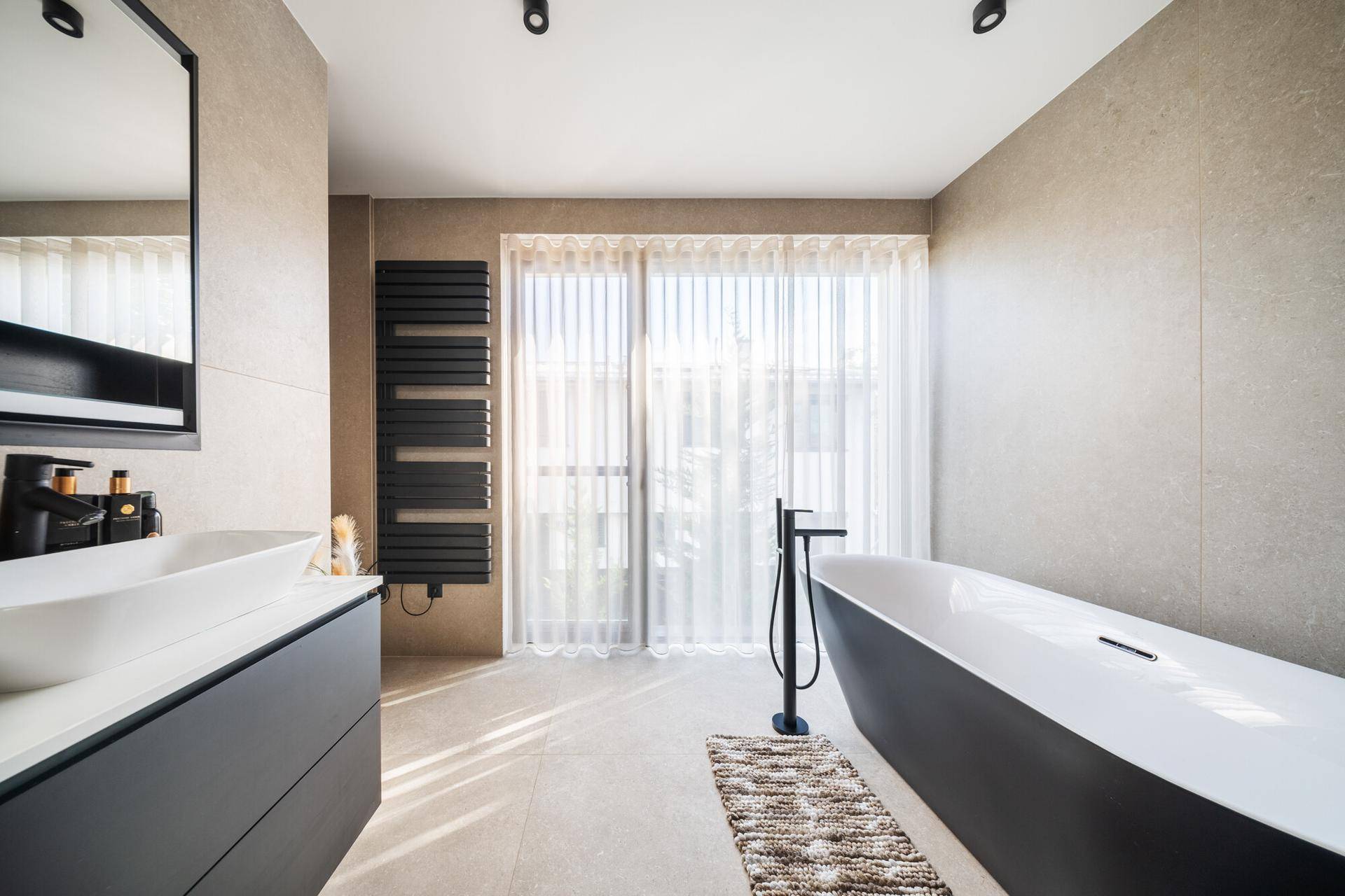 Elegantes Badezimmer mit freistehender Badewanne, beheiztem Handtuchhalter und großen Fenstern.