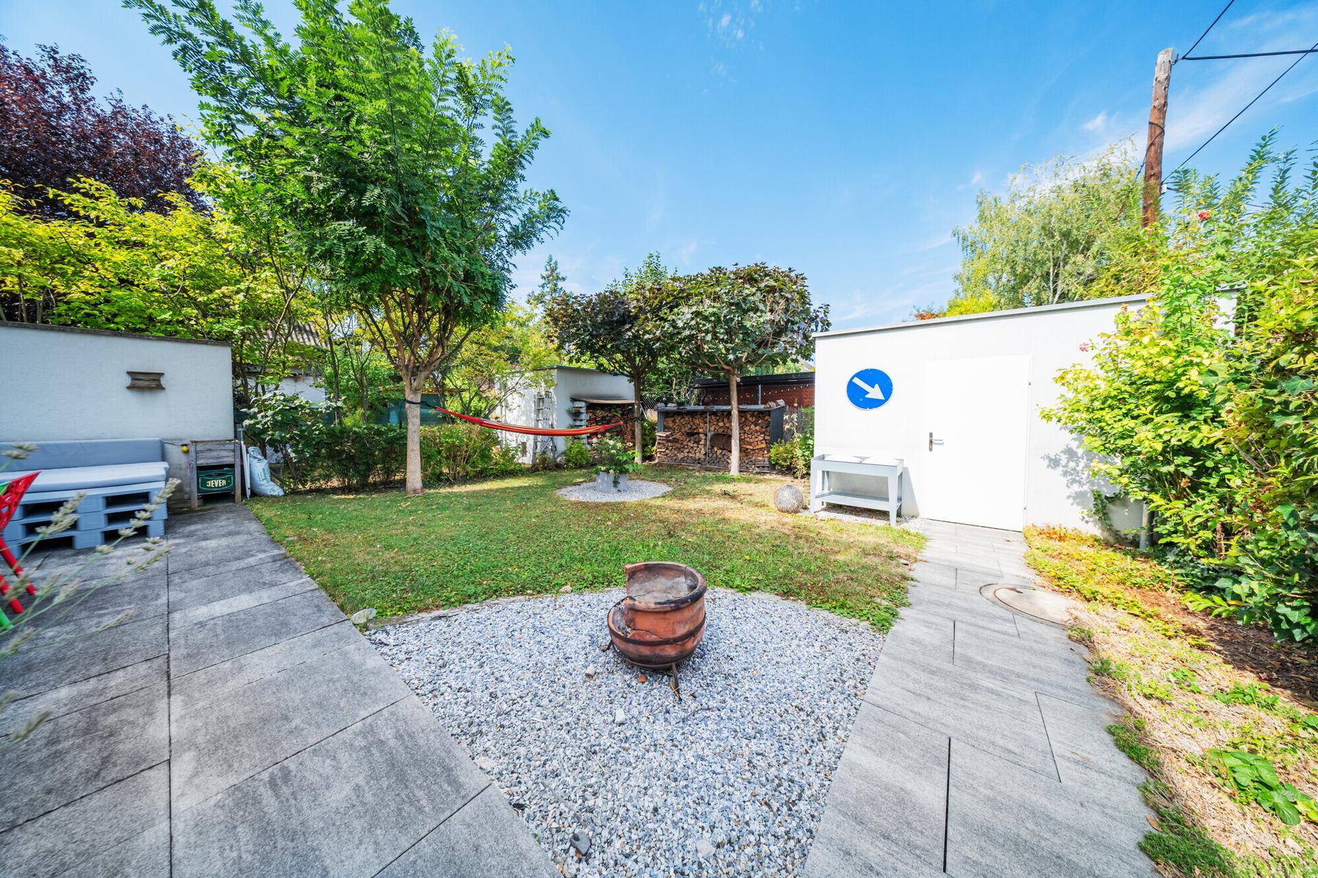 Gepflegter Garten mit Rasenfläche, Kiesbereich, Bäumen und einem praktischen Gartenhaus.