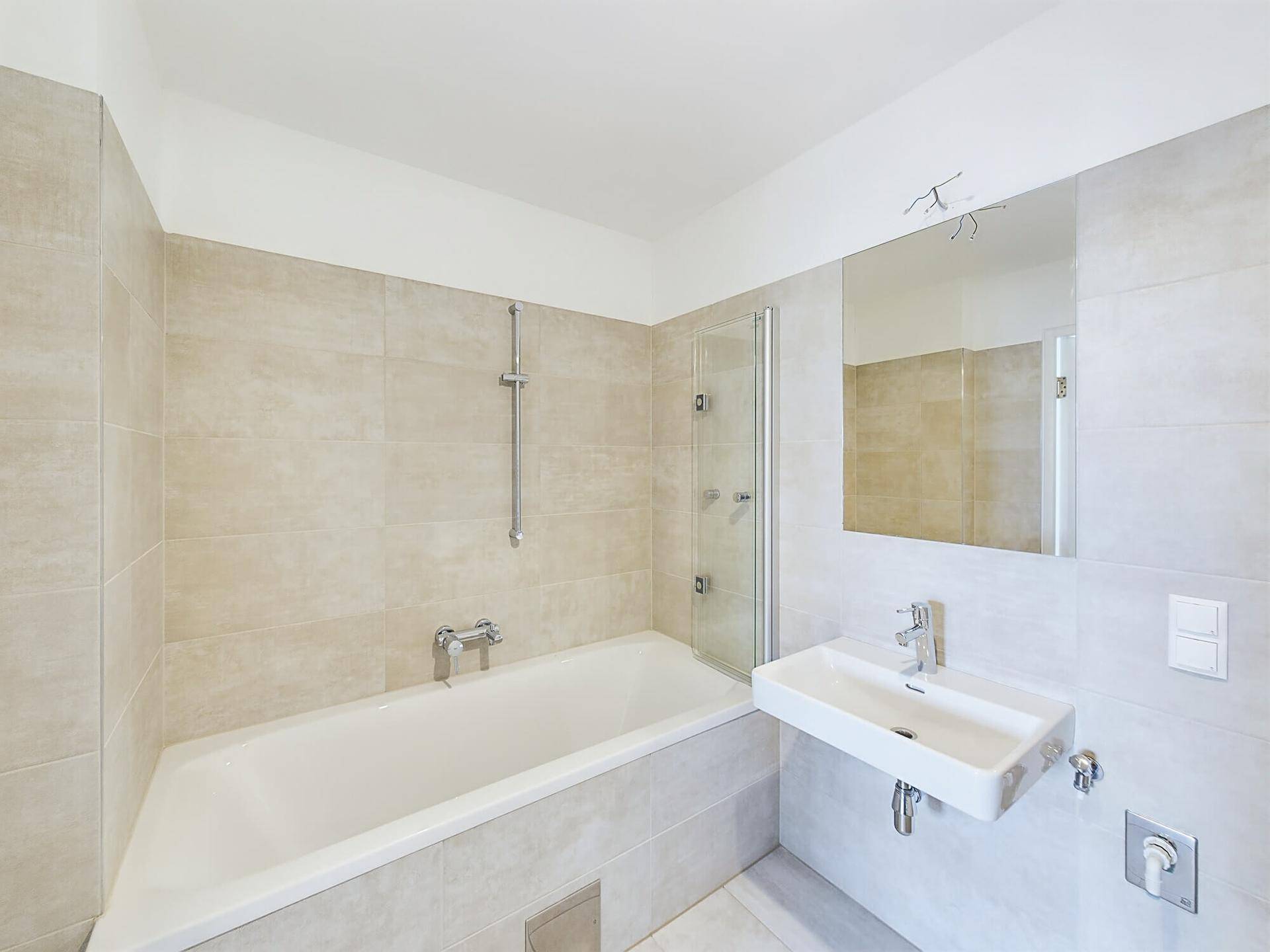 Modernes Badezimmer mit beigefarbenen Fliesen, Badewanne und integrierter Dusche.