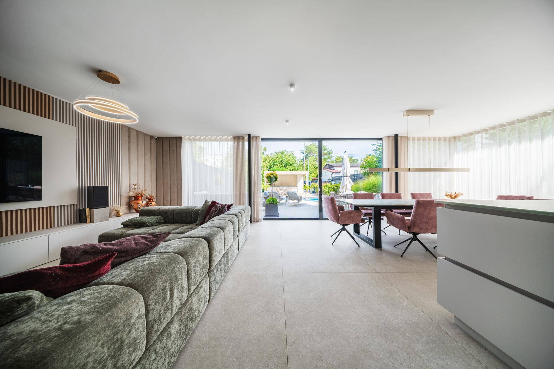 Heller, offener Wohn- und Essbereich mit großem Sofa, modernen Fliesen und Zugang zur Terrasse.