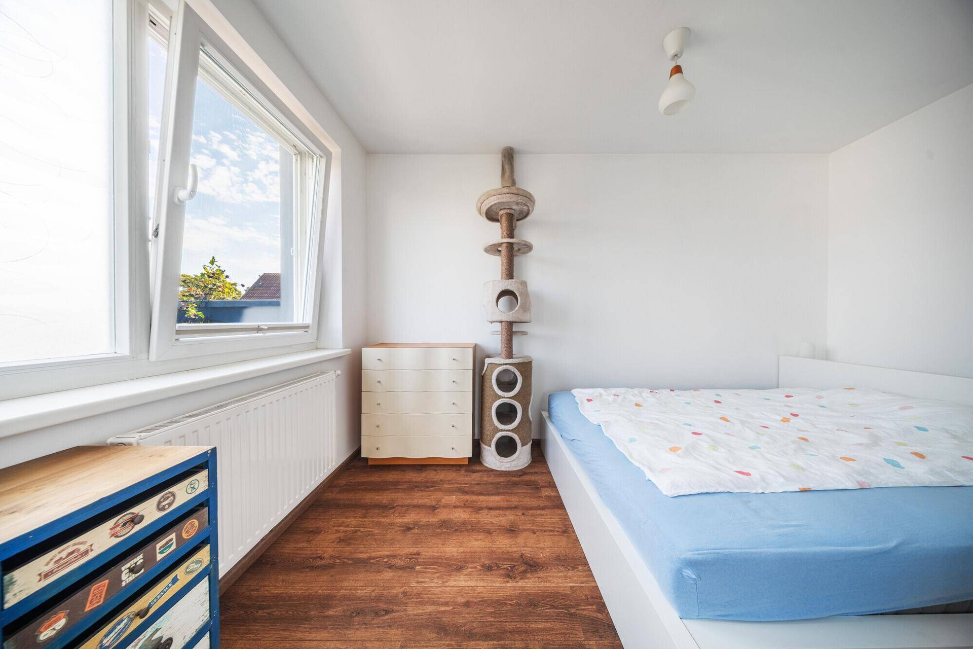 Helles Schlafzimmer mit Holzboden, großem Fenster und einem hohen Katzenkratzbaum.