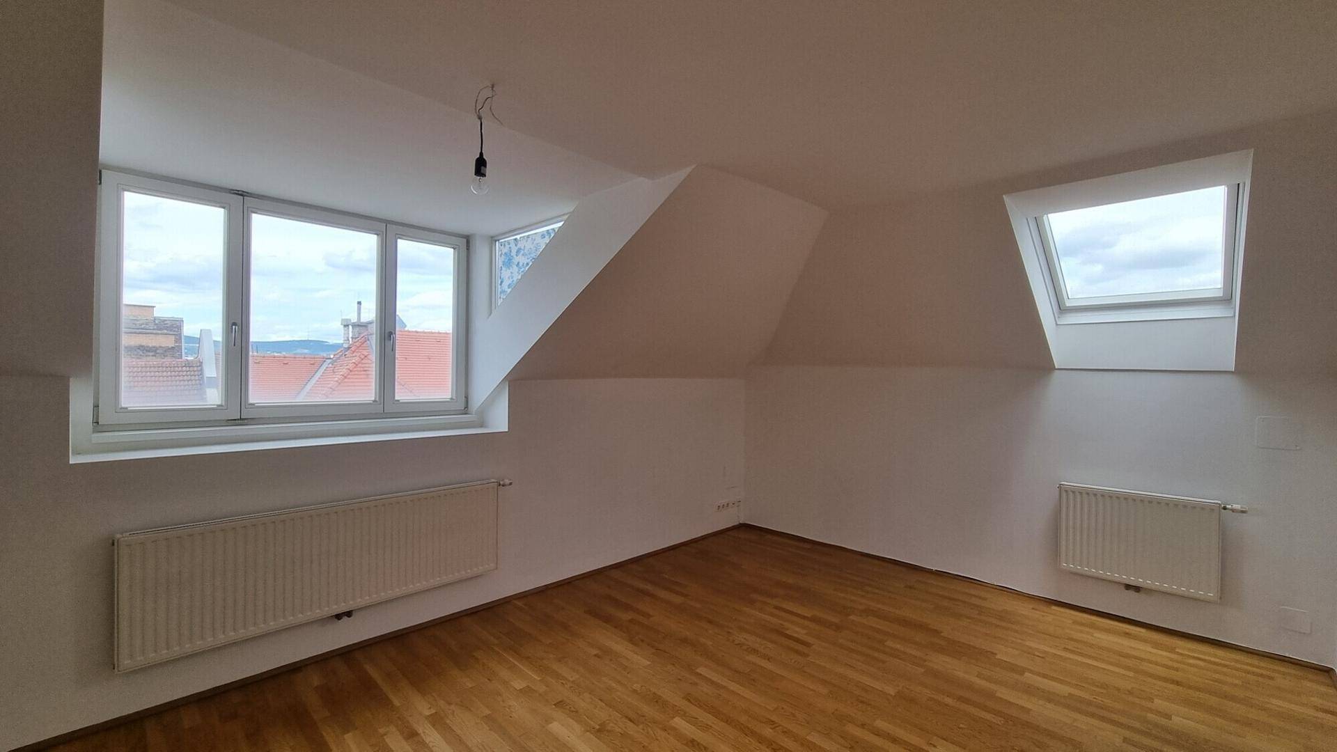 Helles Schlafzimmer im Dachgeschoss mit Holzboden, großem Fenster und Dachfenster.