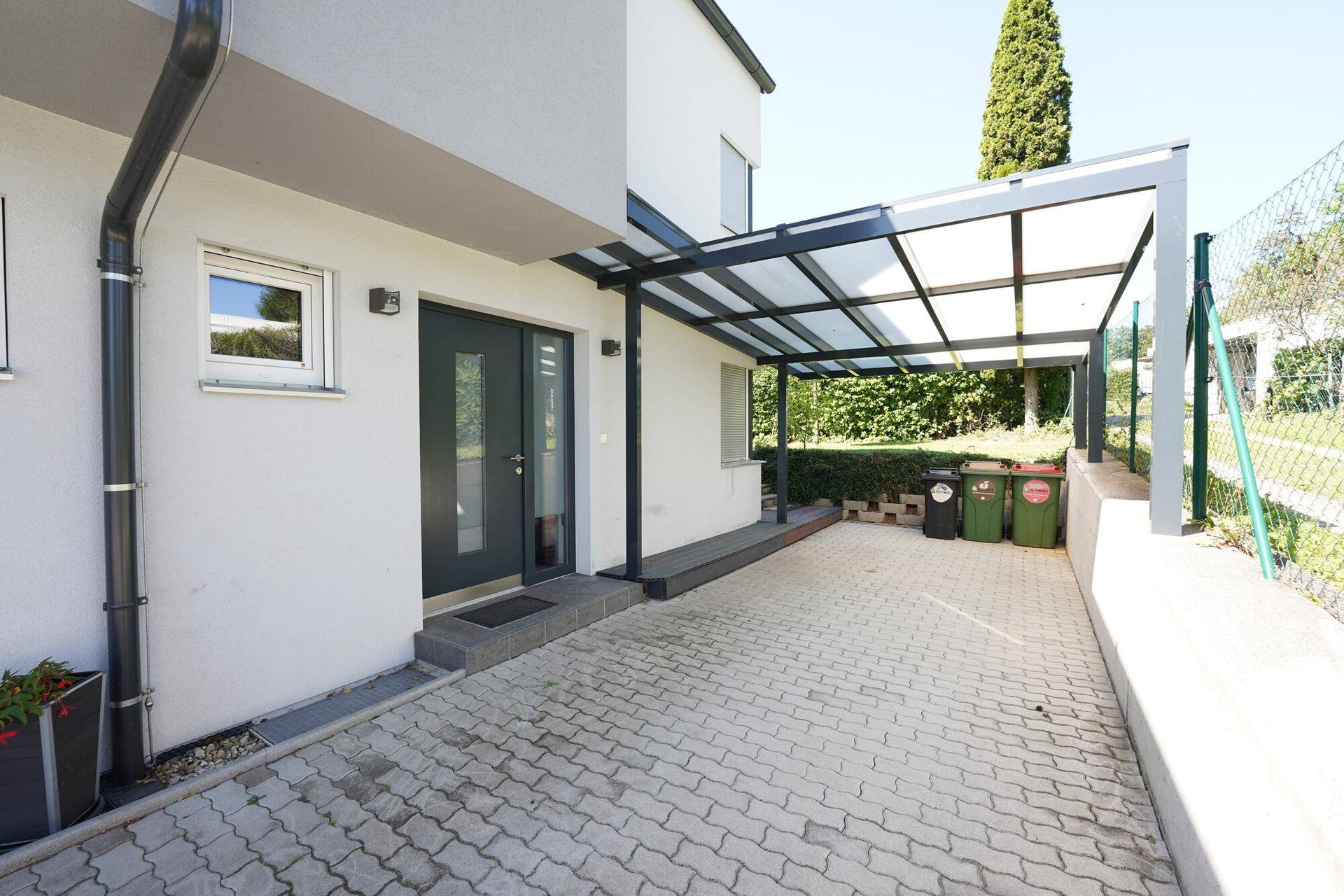 Moderner Hauseingang mit Carport und gepflasterter Auffahrt, bietet praktischen Zugang.