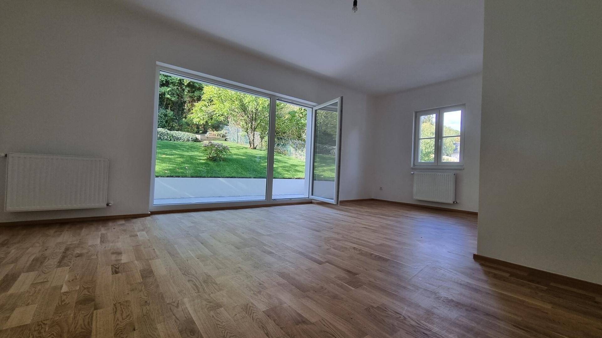 Helles Wohnzimmer mit Eichenparkett und großen Glasfenstern zum Garten.