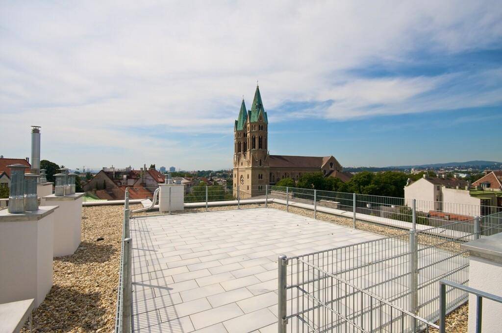 Weitläufige Dachterrasse mit hellen Fliesen und einem beeindruckenden Blick auf eine Kirche und die Stadt.