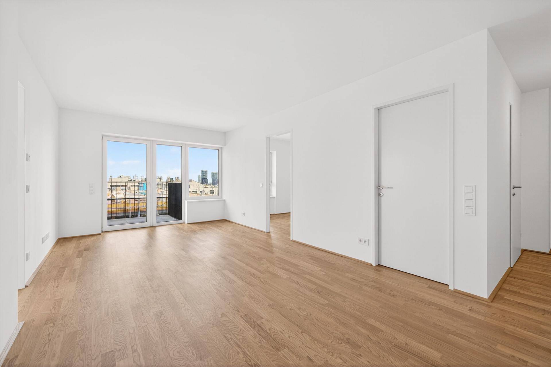 Großes, helles Wohnzimmer mit Holzboden und Zugang zu einem Balkon.