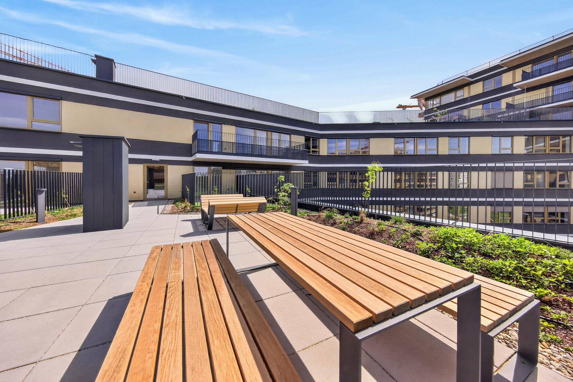 Moderne Dachterrasse mit Holzbänken und Tischen, umgeben von zeitgenössischer Architektur und Grünflächen.