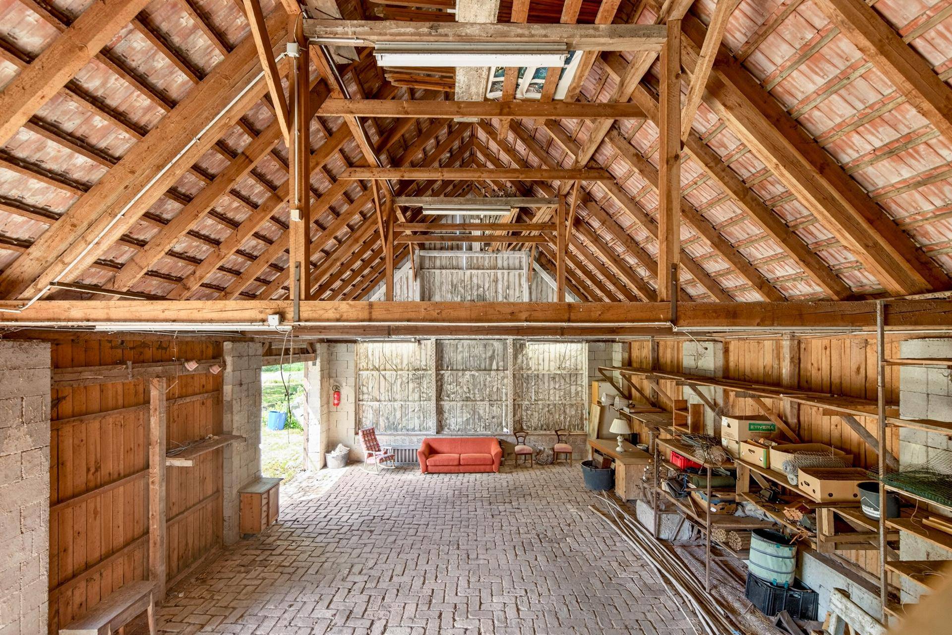Geräumiger Innenraum einer Scheune mit hohen Holzdecken, Ziegelboden und Lagerregalen.