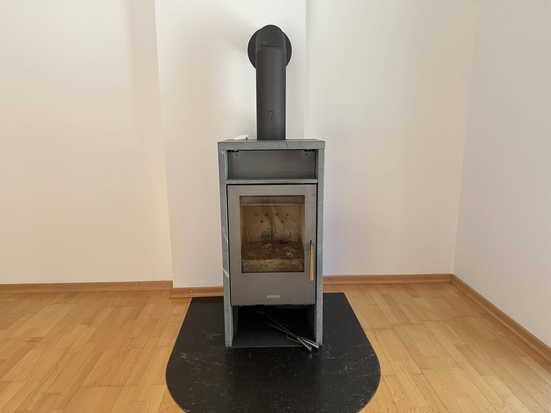 Moderner Kaminofen auf dunkler Bodenplatte, bereit für gemütliche Stunden im Wohnzimmer.