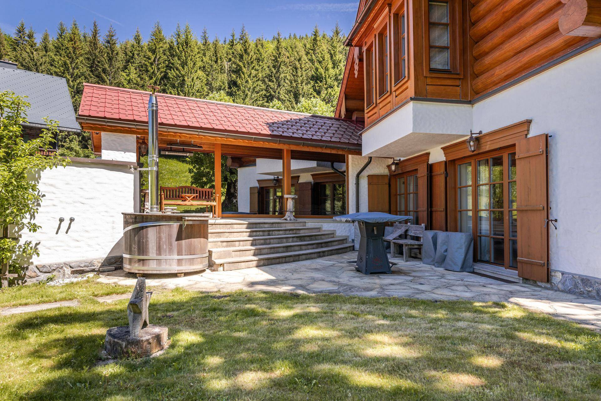 Große Steinterrasse mit Holz-Whirlpool, überdachtem Bereich und Zugang zum Garten.