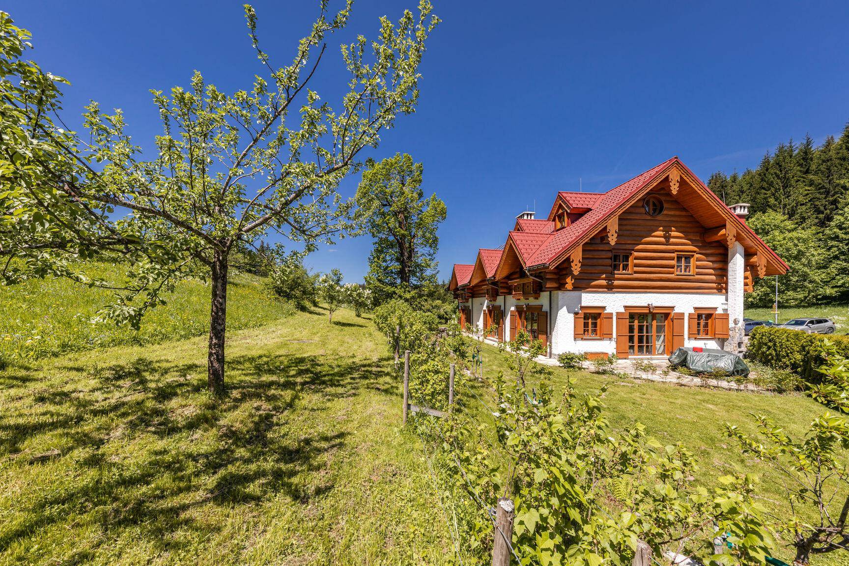 Charmantes Holzhaus mit rotem Dach, umgeben von einem grünen Garten und Obstbäumen.