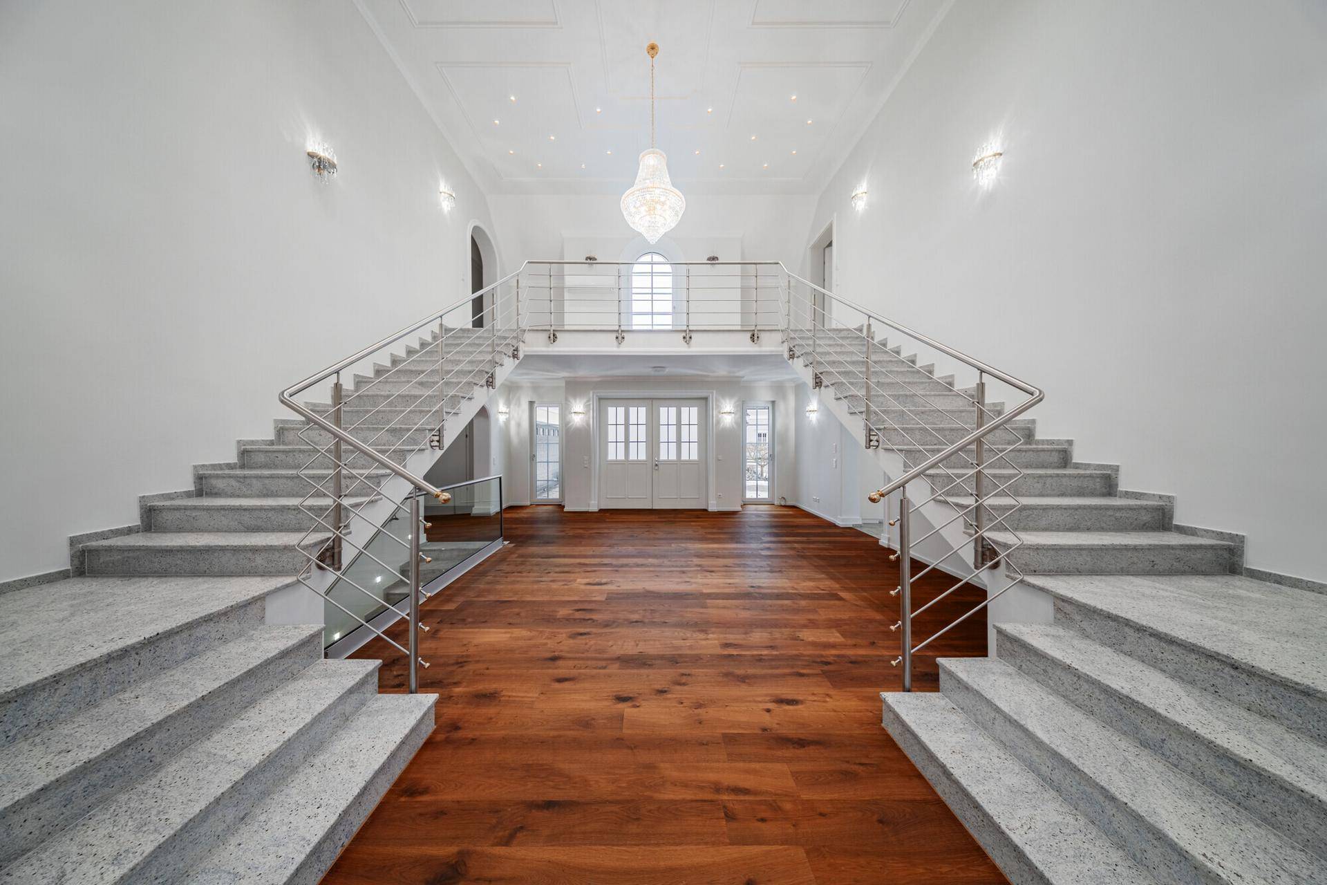 Repräsentativer Eingangsbereich mit doppelter Marmortreppe, hohen Decken und Holzboden.