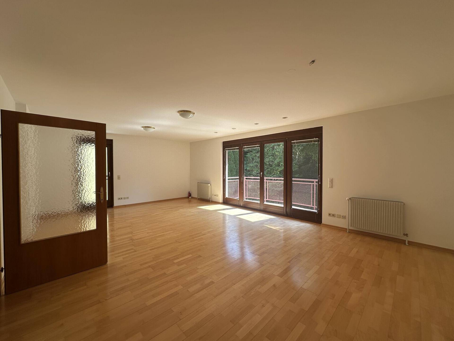 Geräumiges Wohnzimmer mit Holzboden und großen Fenstern, die den Raum erhellen.