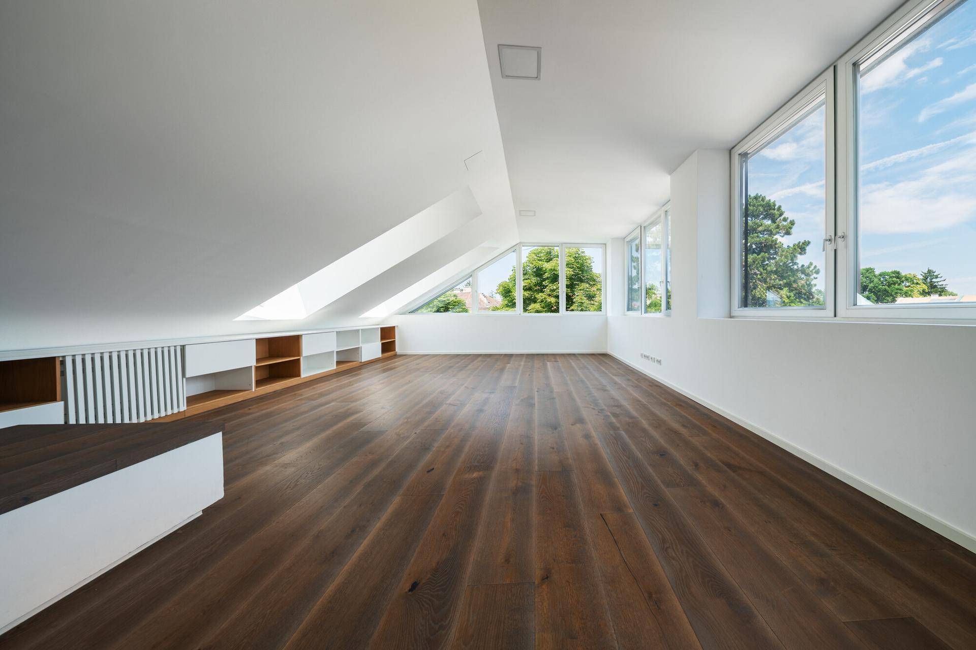 Weitläufiger Dachbodenraum mit Holzdielenboden, schrägen Decken und integrierten Regalen unter den Fenstern.