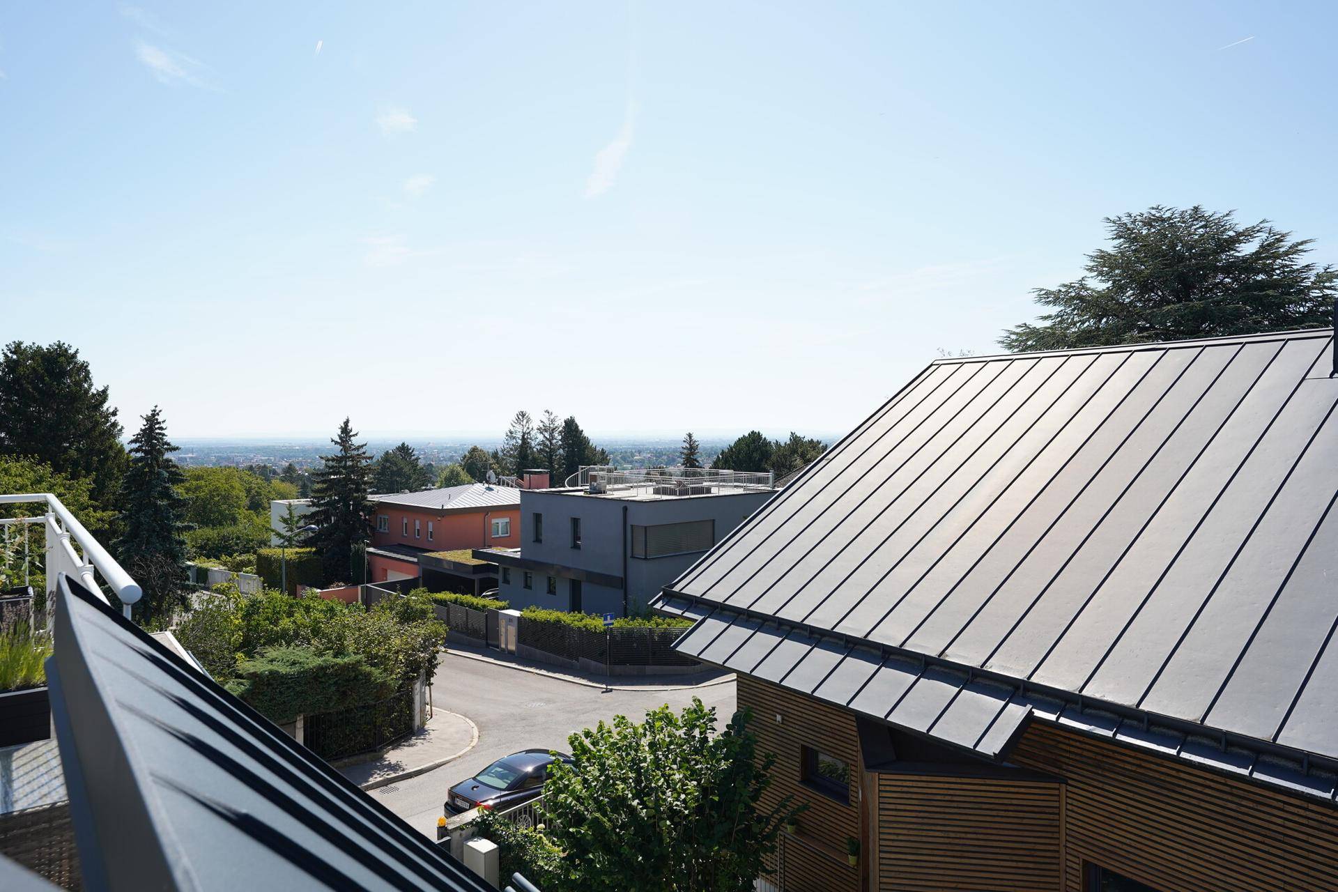 Weitblick über Dächer und Bäume bis zur Ferne, von einem sonnigen Balkon aus genossen.