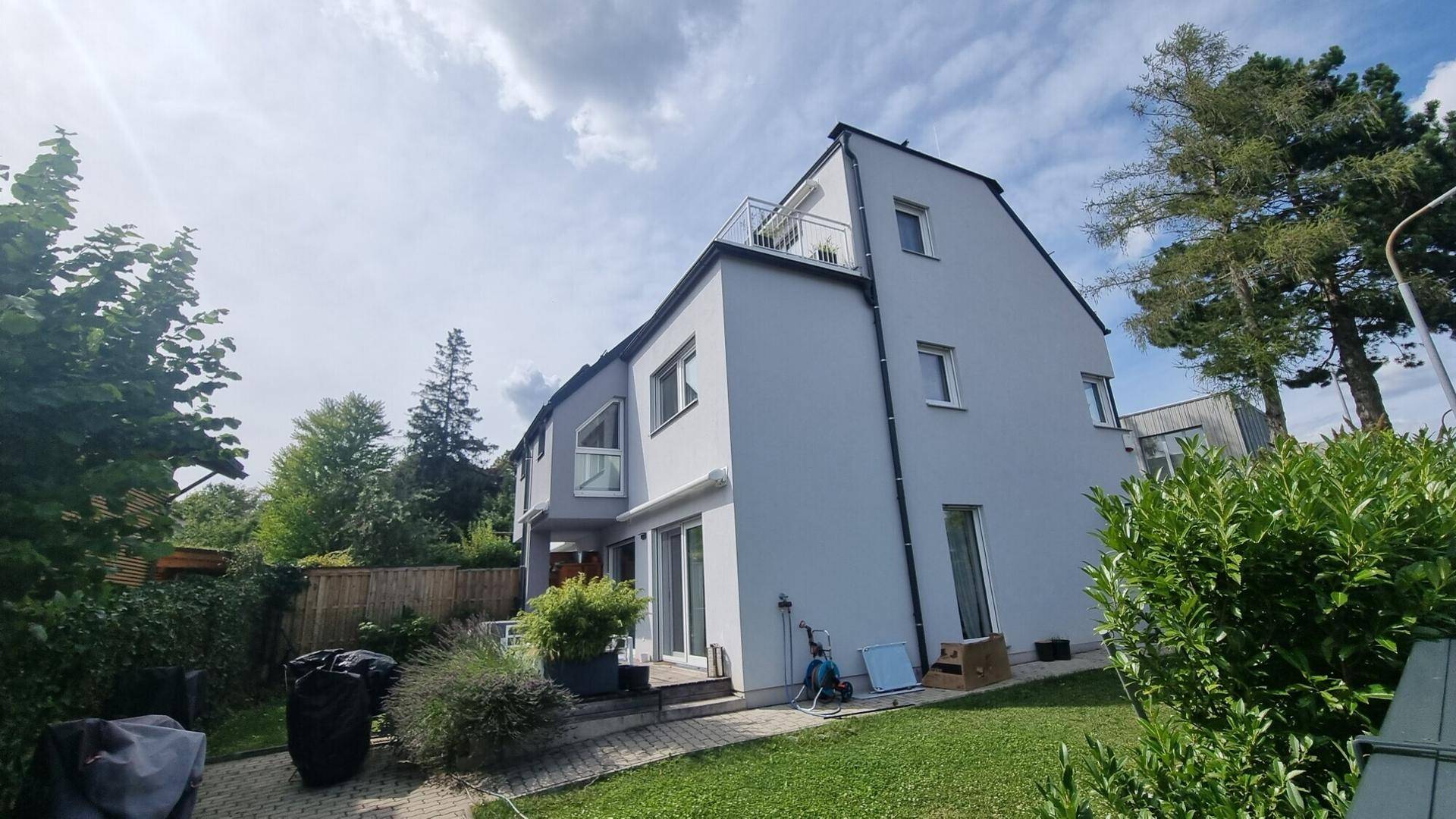 Rückansicht des modernen Hauses mit Balkon, Terrasse und gepflegtem Gartenbereich.