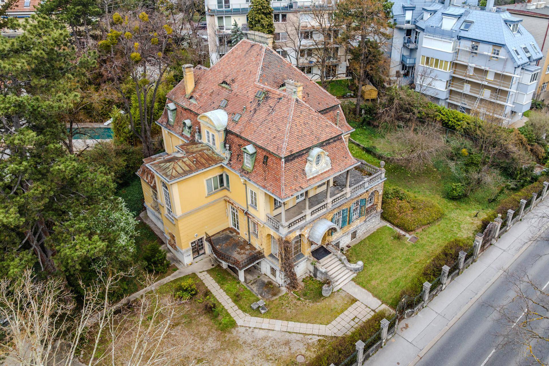 Luftaufnahme der historischen Villa mit weitläufigem Grundstück, Mansarddach und umliegender Bebauung.