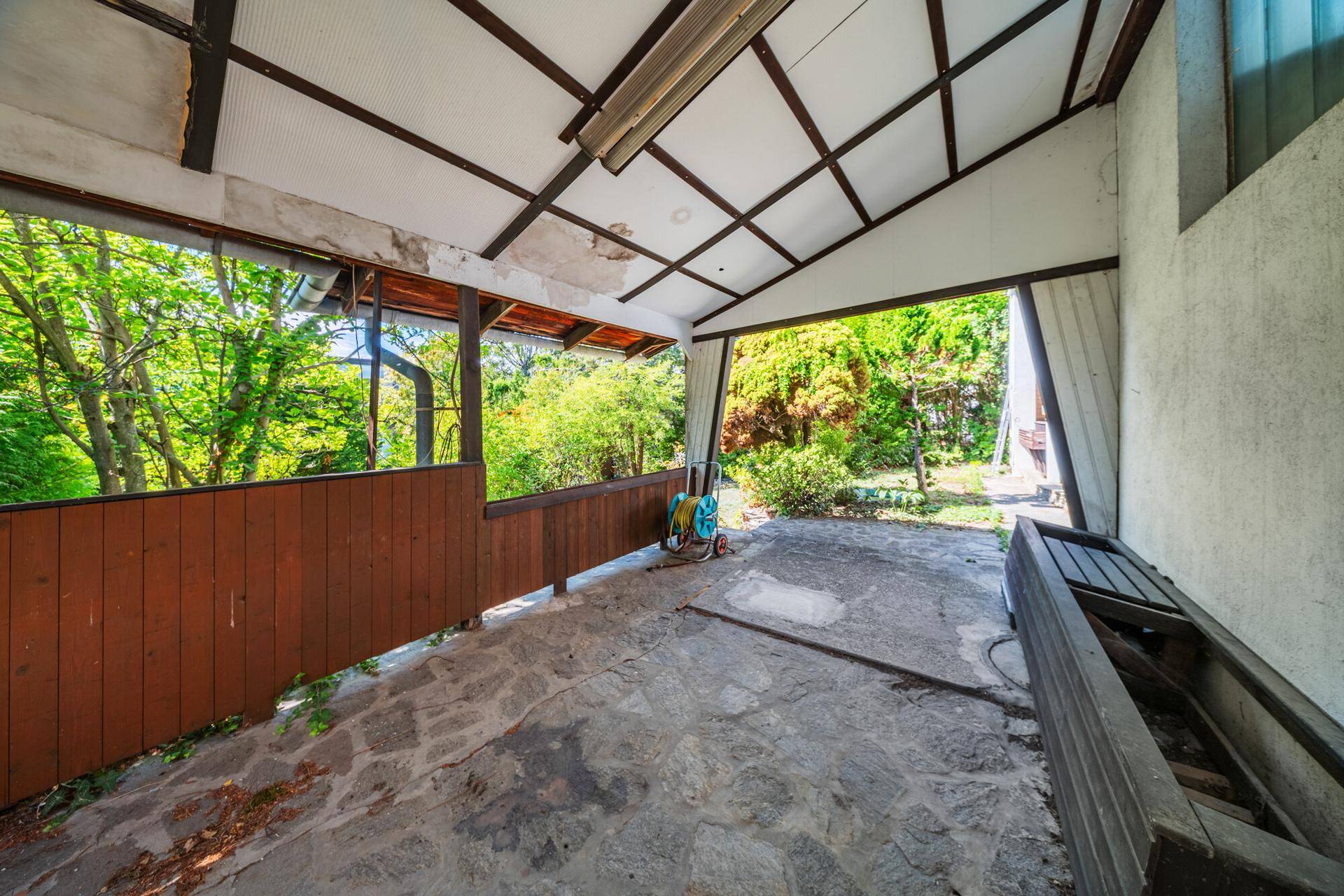 Überdachte Terrasse mit Steinboden und Blick in den grünen Gartenbereich, ideal für Mahlzeiten im Freien.