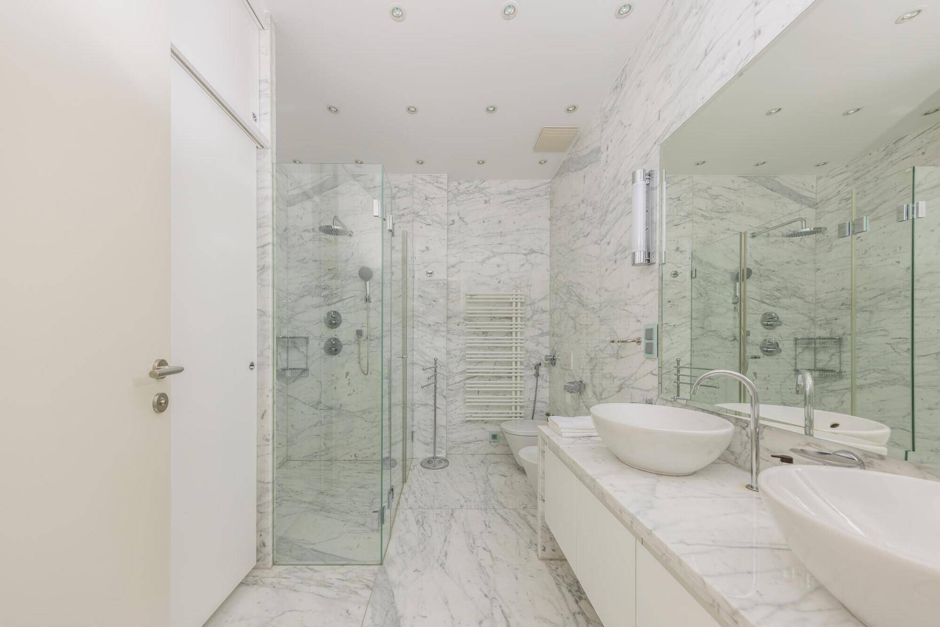 Luxuriöses Badezimmer mit Marmorfliesen, begehbarer Dusche und Doppelwaschbecken.