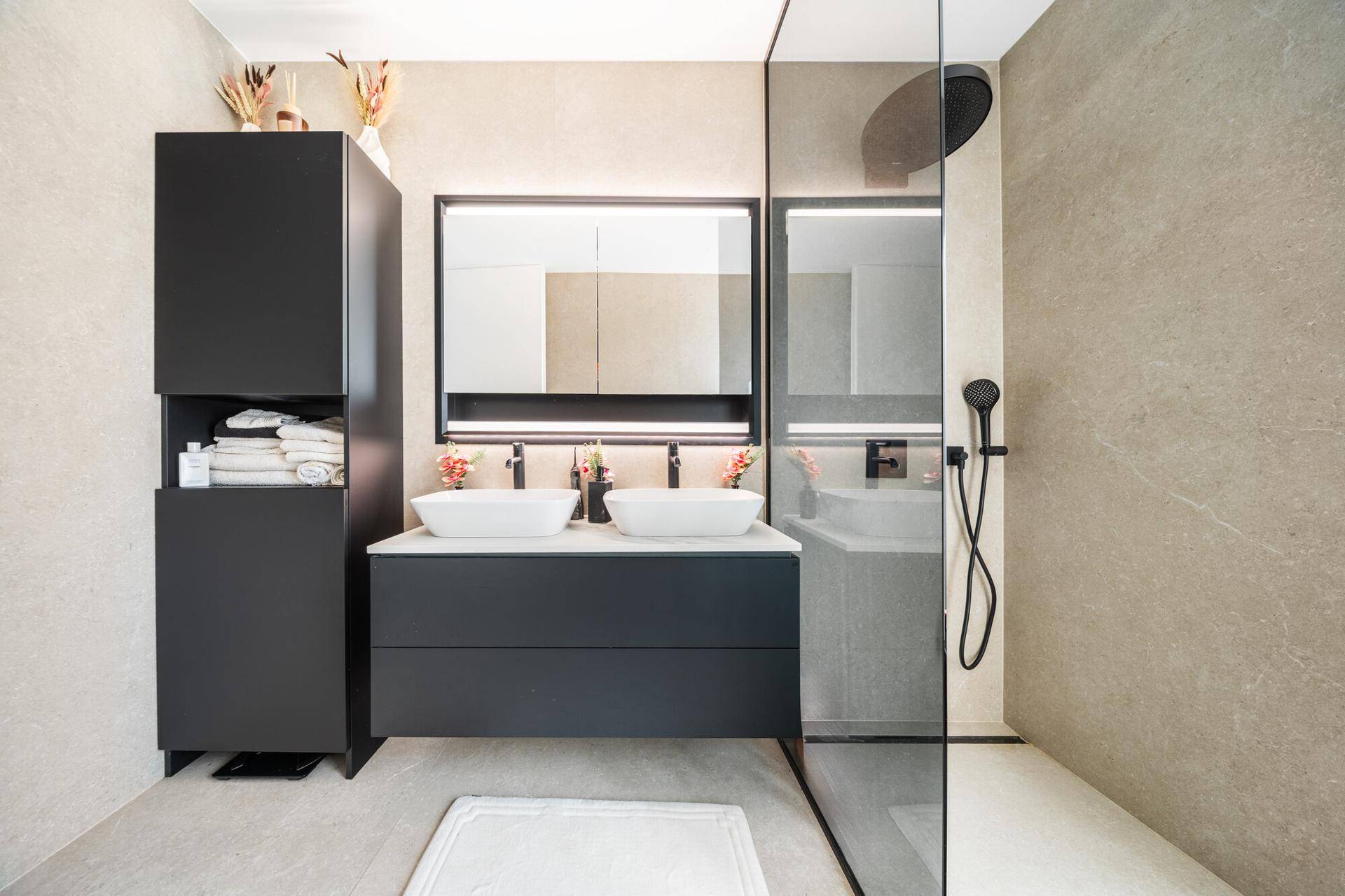 Modernes Badezimmer mit Doppelwaschbecken, begehbarer Dusche und dunklen Schränken.