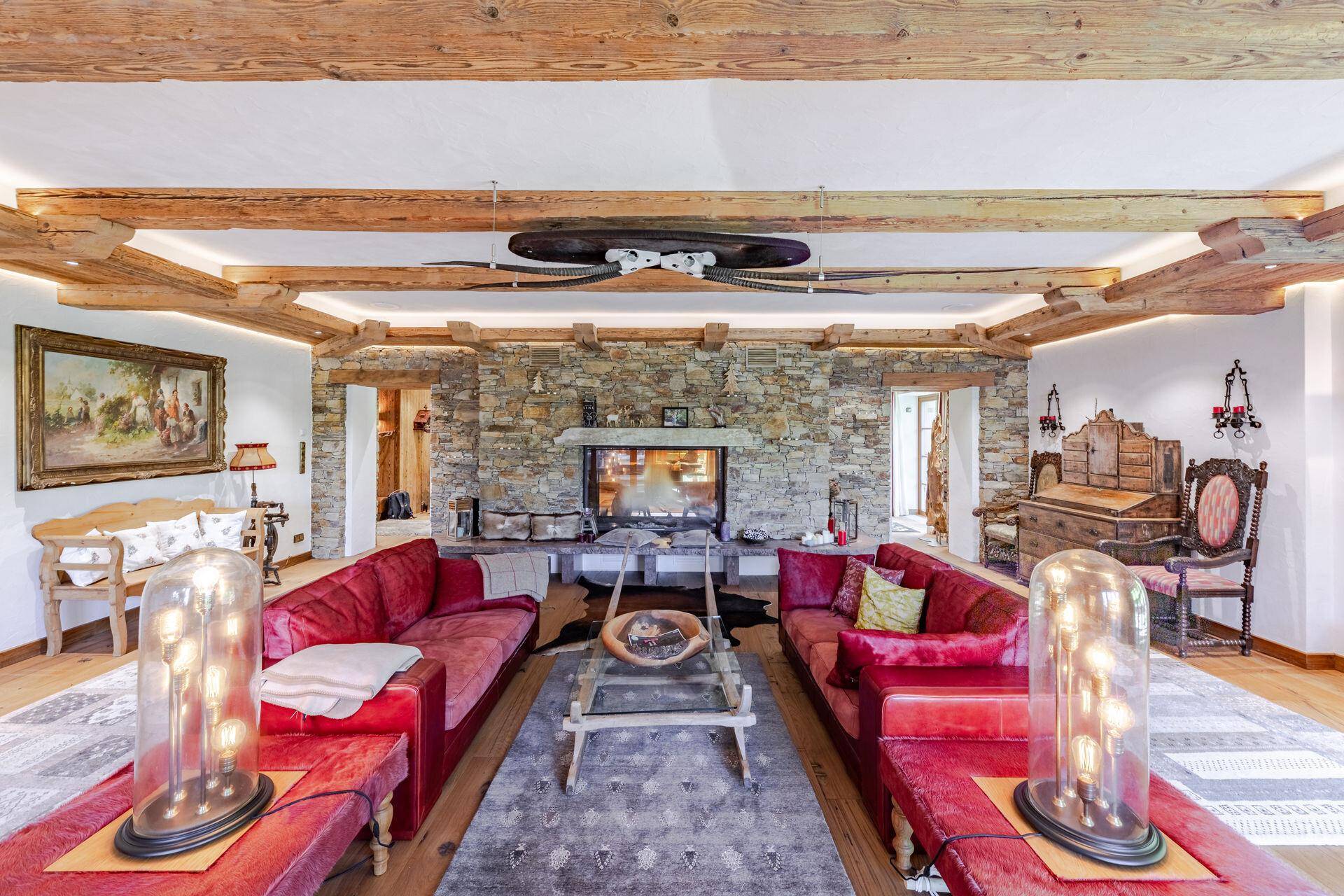 Elegantes Wohnzimmer mit Steinkamin, roten Sofas und Holzbalkendecke.