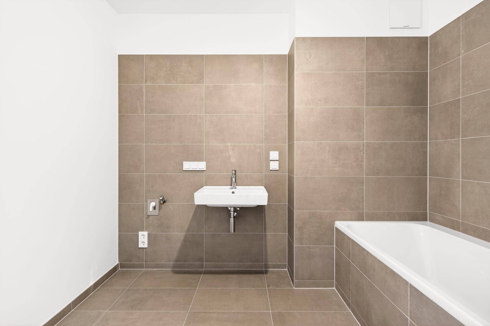 Modernes Badezimmer mit braunen Fliesen, weißem Waschbecken und Badewanne.