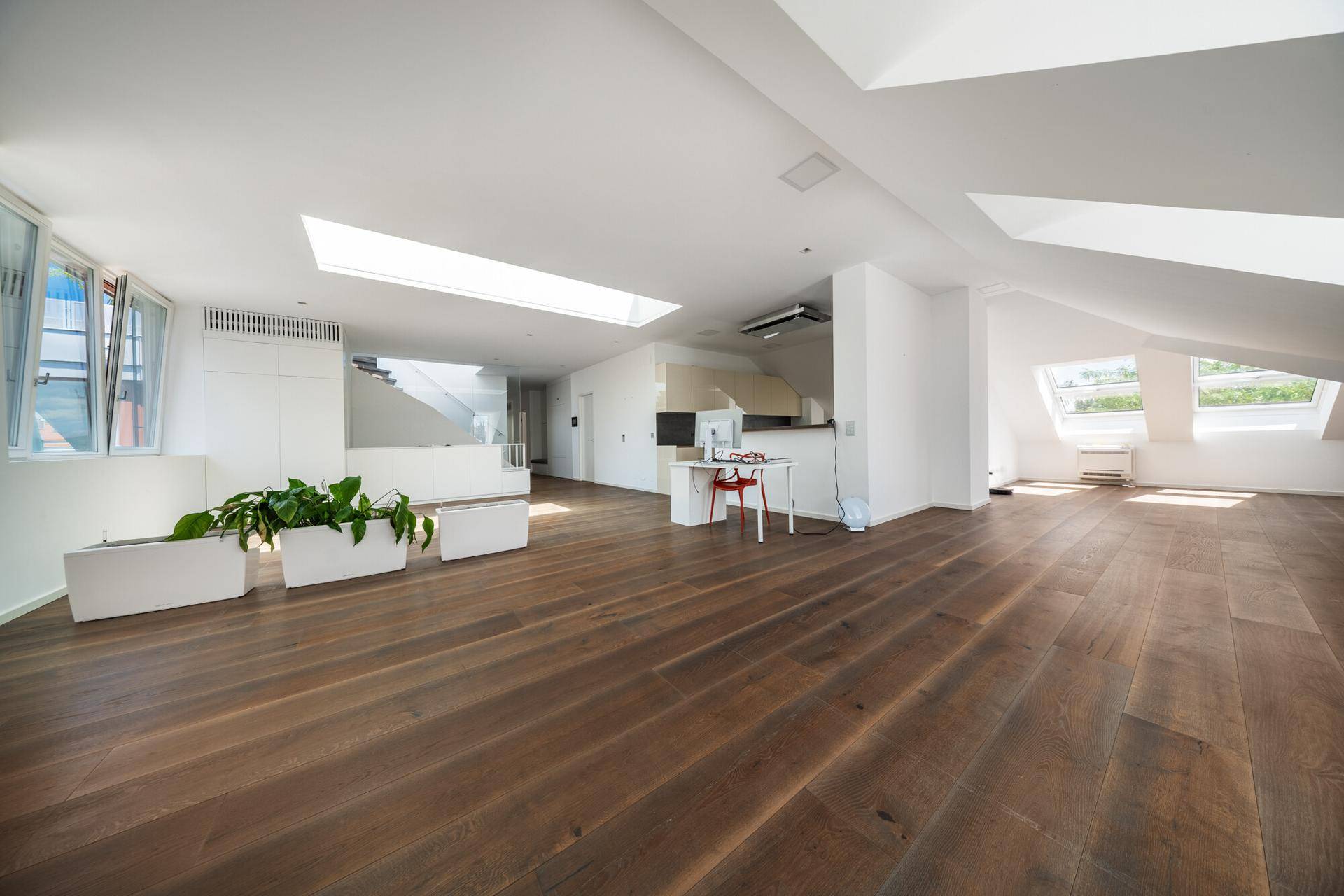 Großzügiger, offener Wohnbereich mit Holzdielenboden, Oberlicht und einer modernen Treppe im Hintergrund.