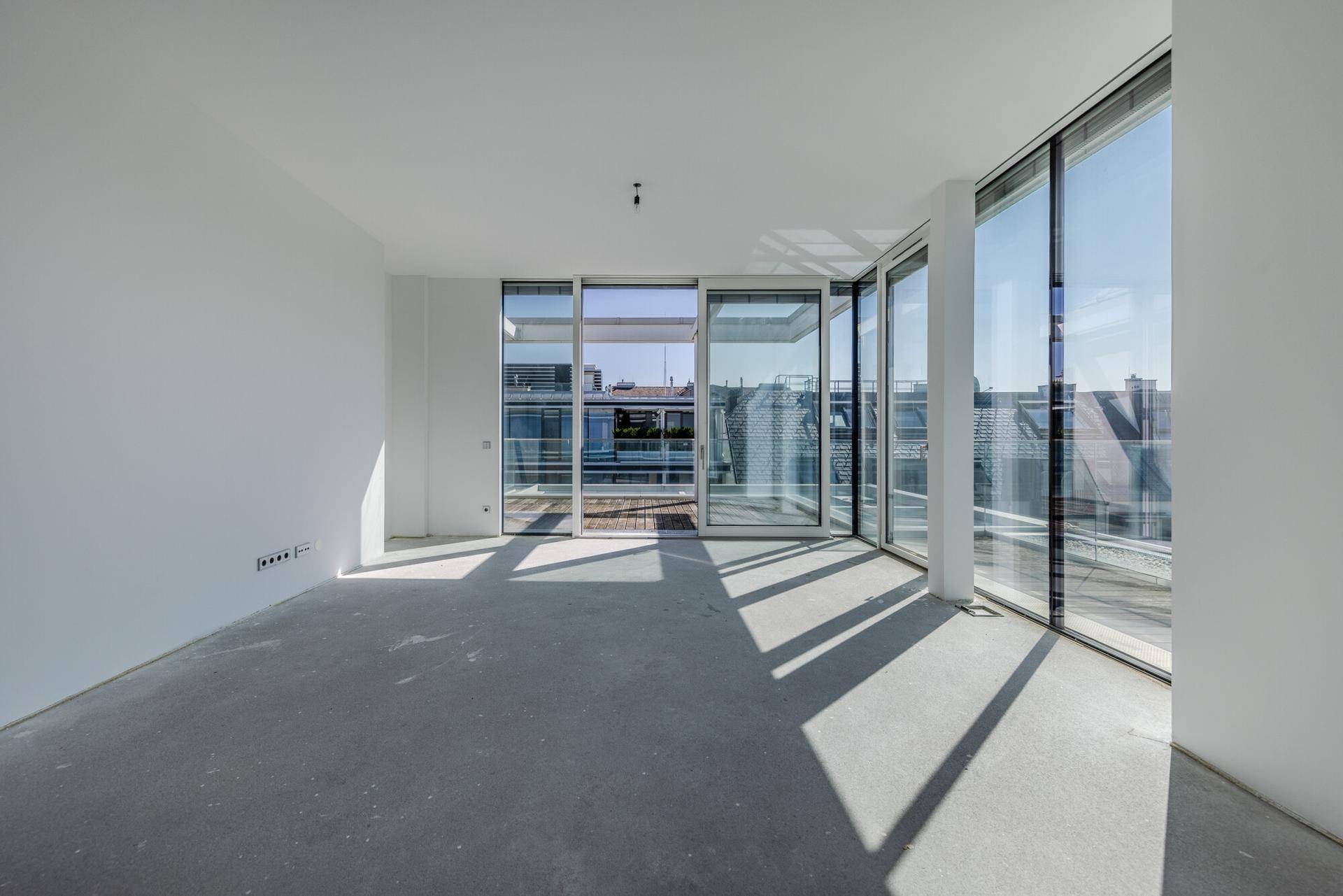 Lichtdurchfluteter, unmöblierter Raum mit Betonboden und Zugang zur Dachterrasse.