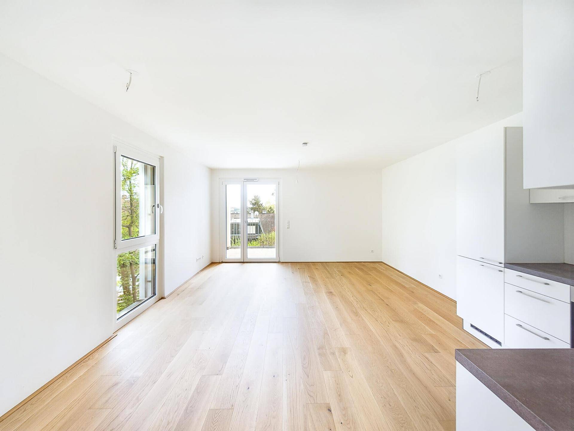 Heller, offener Wohnbereich mit Eichenparkett und Zugang zu einem Balkon.