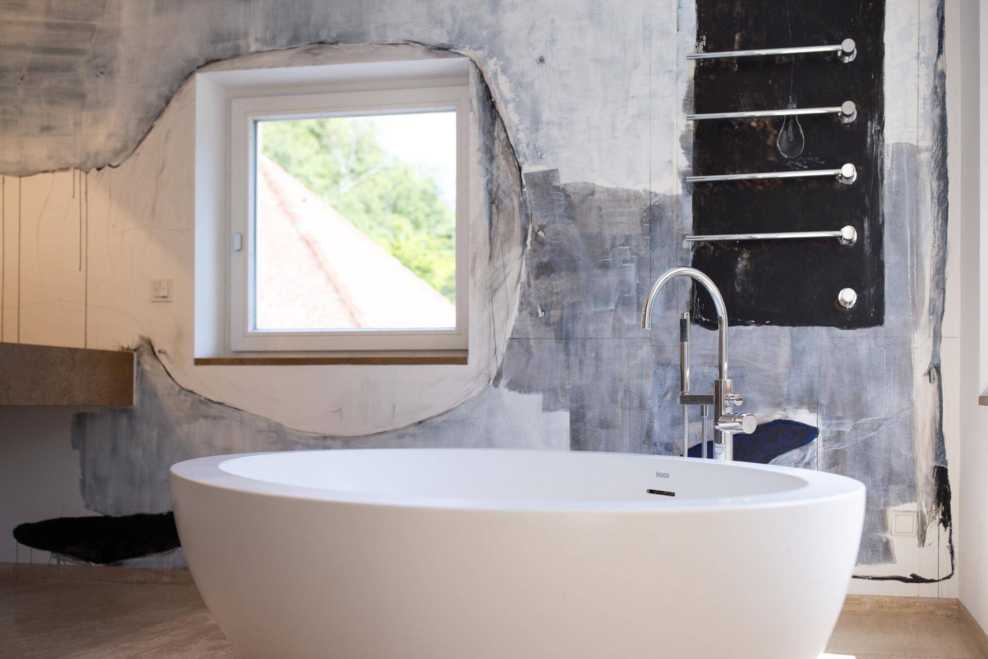 Freistehende Badewanne in einem modernen Badezimmer mit künstlerischer Wandgestaltung und Fenster.