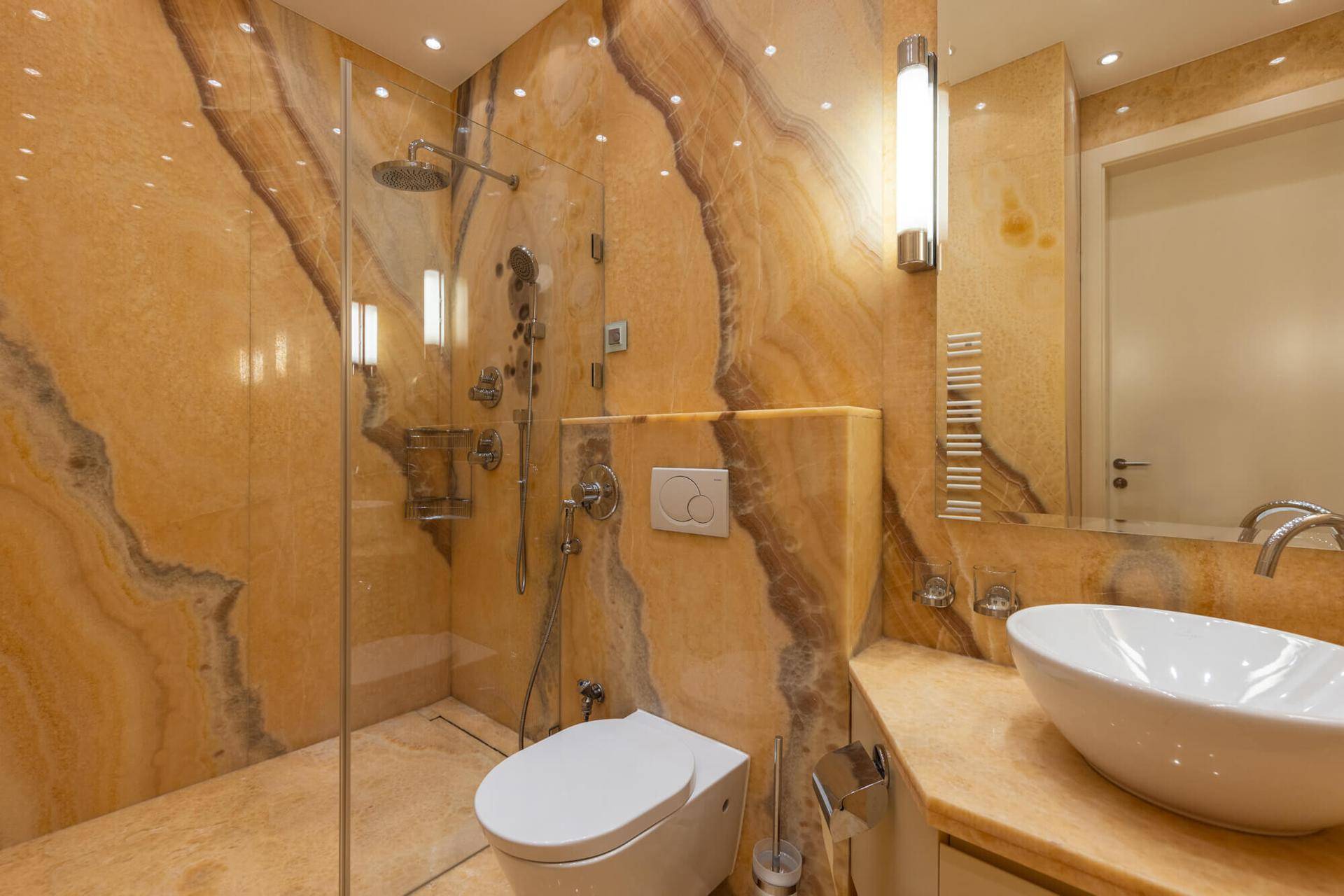 Luxuriöses Badezimmer mit auffälligen Marmorwänden, begehbarer Dusche und modernem Waschbecken.