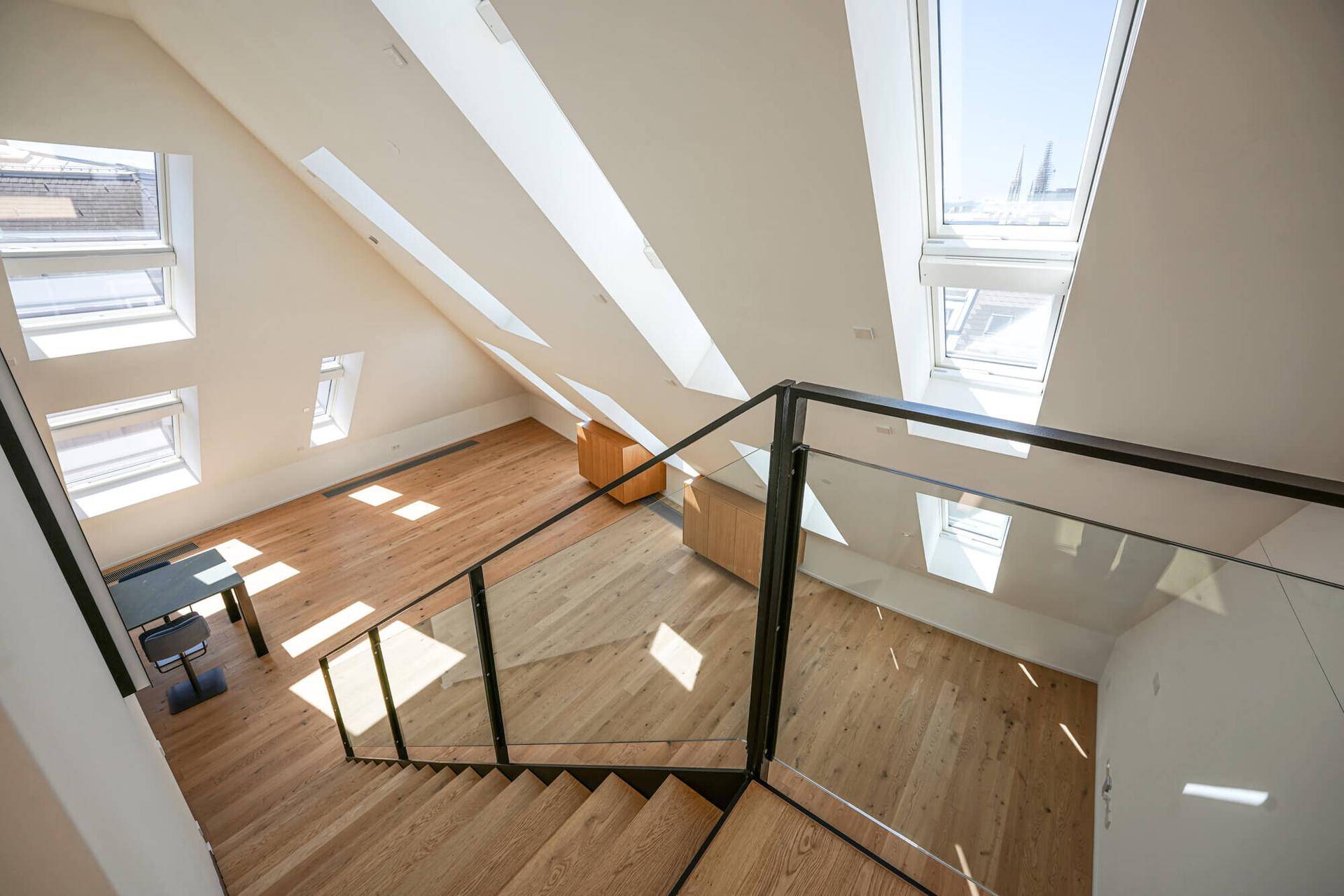 Offener Bereich mit viel Tageslicht durch Dachfenster und moderner Treppe mit Glasgeländer.