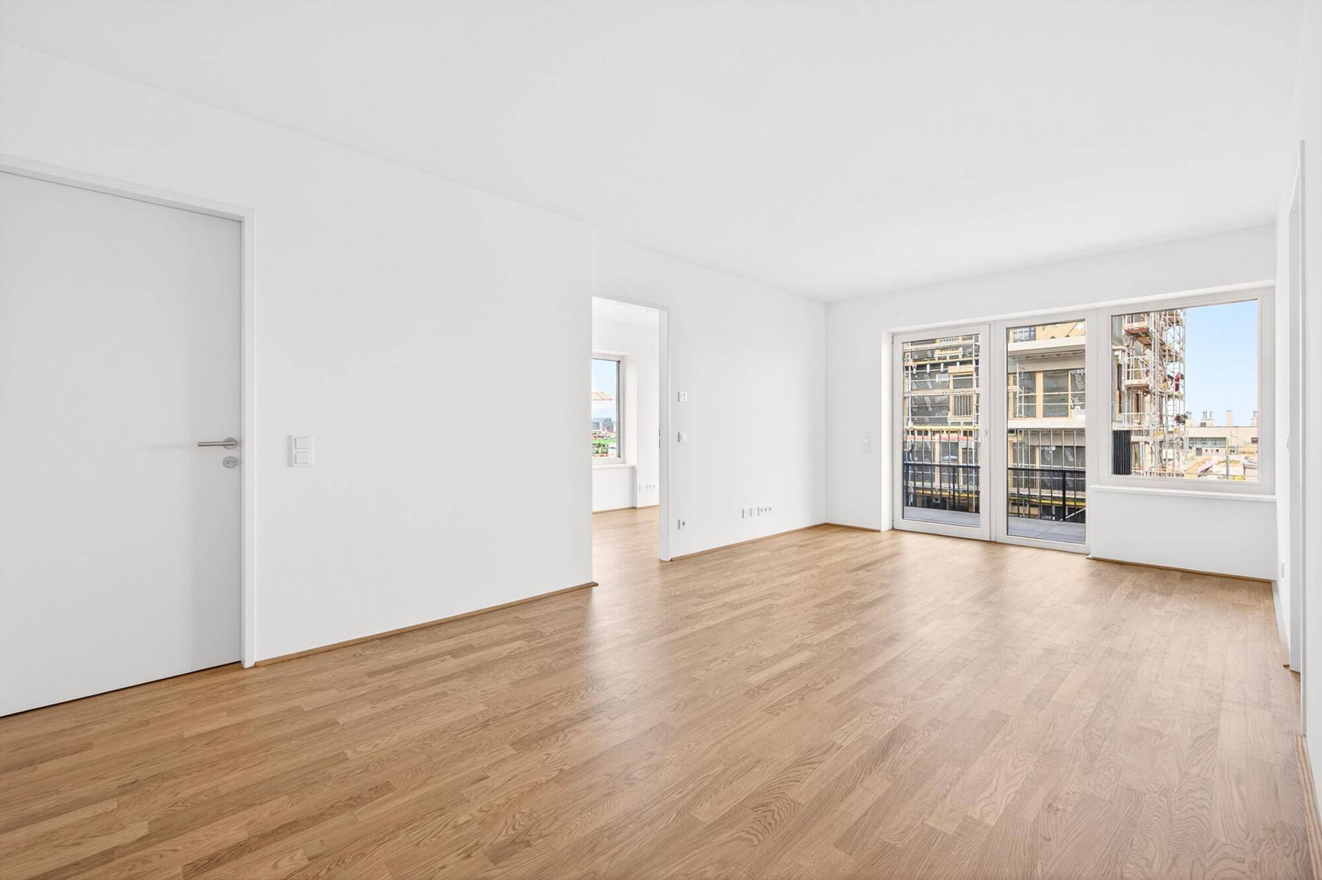 Geräumiges Wohnzimmer mit hellem Parkettboden und großen Fenstern mit Blick auf die Umgebung.