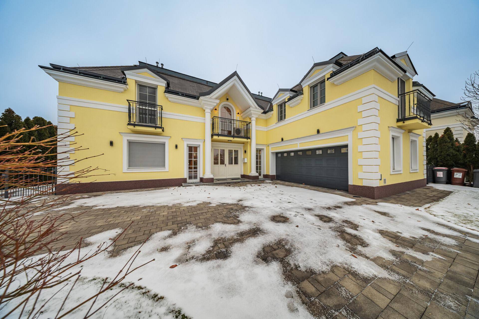 Repräsentative gelbe Villa mit mehreren Balkonen, Garage und gepflasterter Auffahrt.
