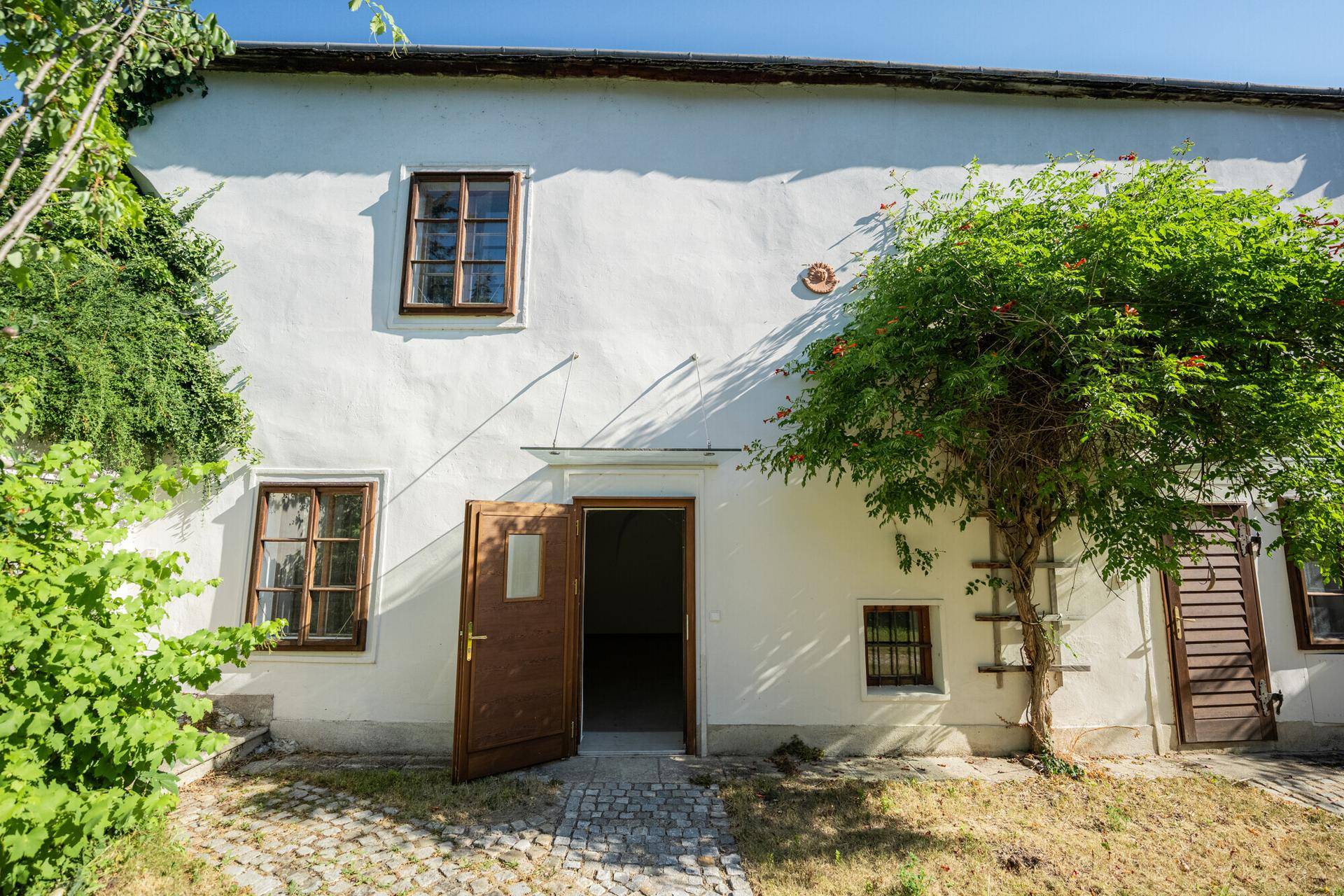 Weiße Fassade eines historischen Gebäudes mit Holztüren und Fenstern im Sonnenlicht.