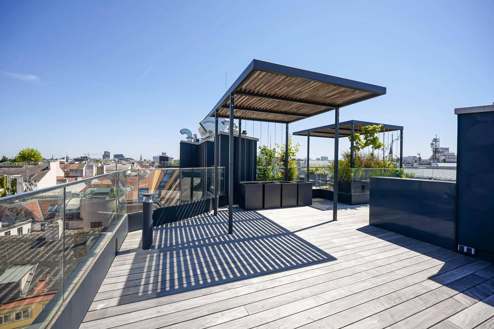 Weitläufige Dachterrasse mit zwei Pergolen und Holzbelag, ideal für Entspannung im Freien.