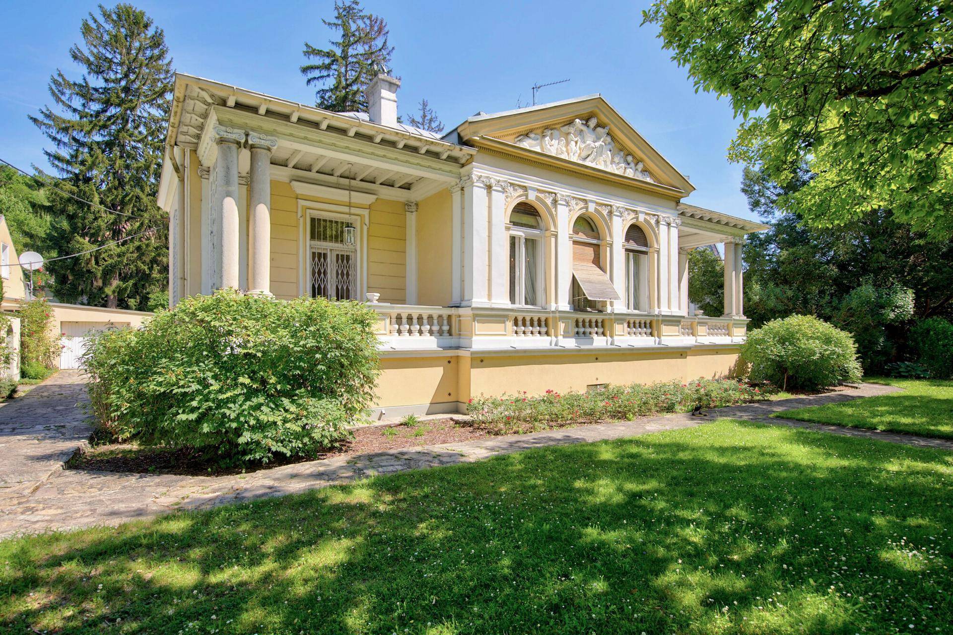 Prächtige Villa mit weitläufigem Garten und klassischer Architektur unter strahlendem Himmel.