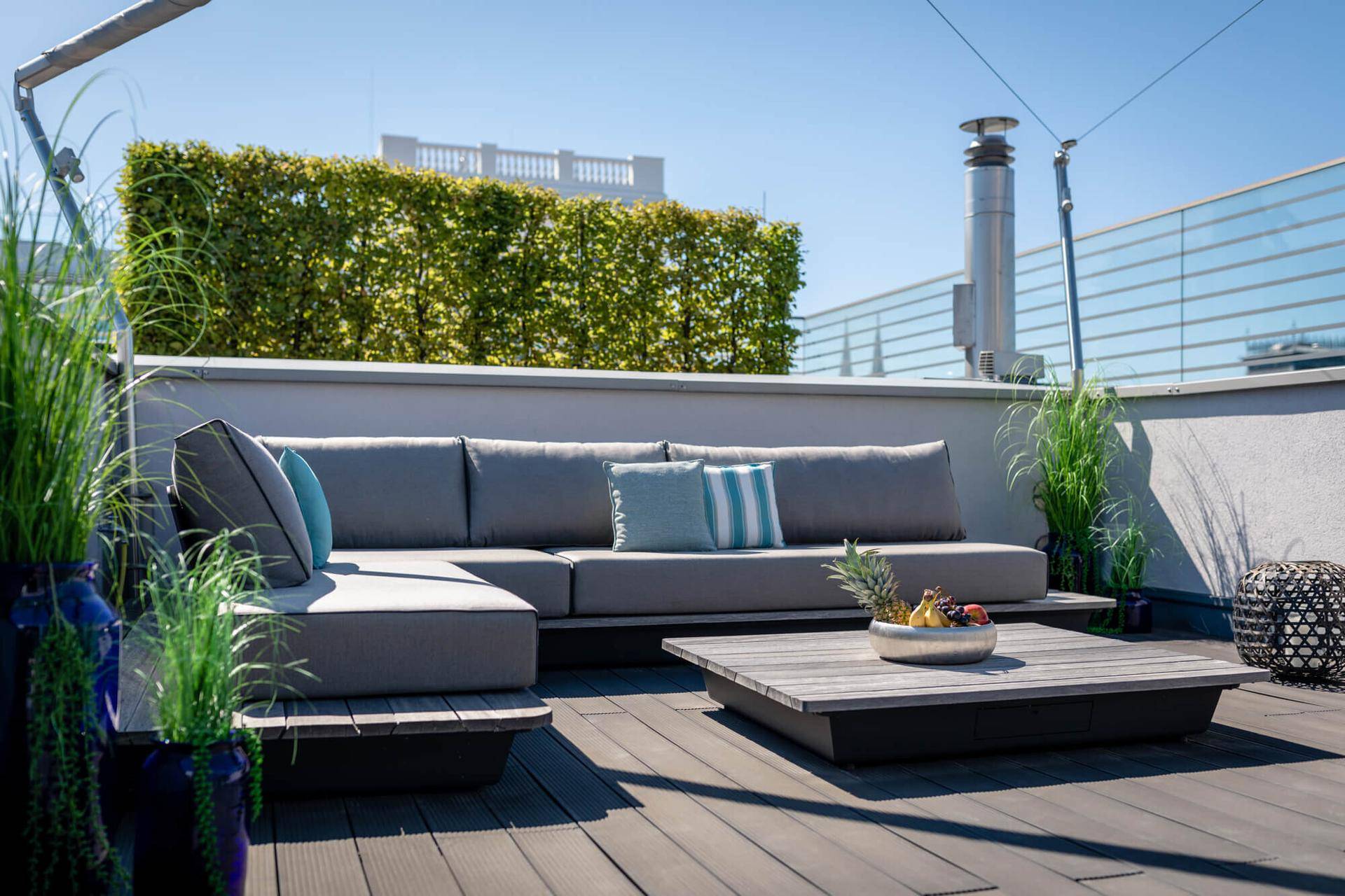 Sonnige Dachterrasse mit bequemen Loungemöbeln und grüner Hecke, perfekt zum Entspannen im Freien.