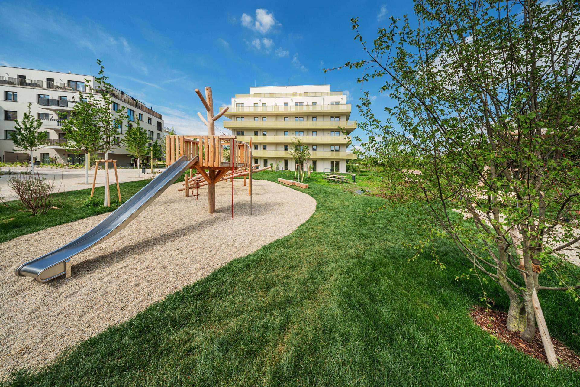 Moderner Kinderspielplatz mit Rutsche und Sandbereich, umgeben von Grünflächen und Wohngebäuden.