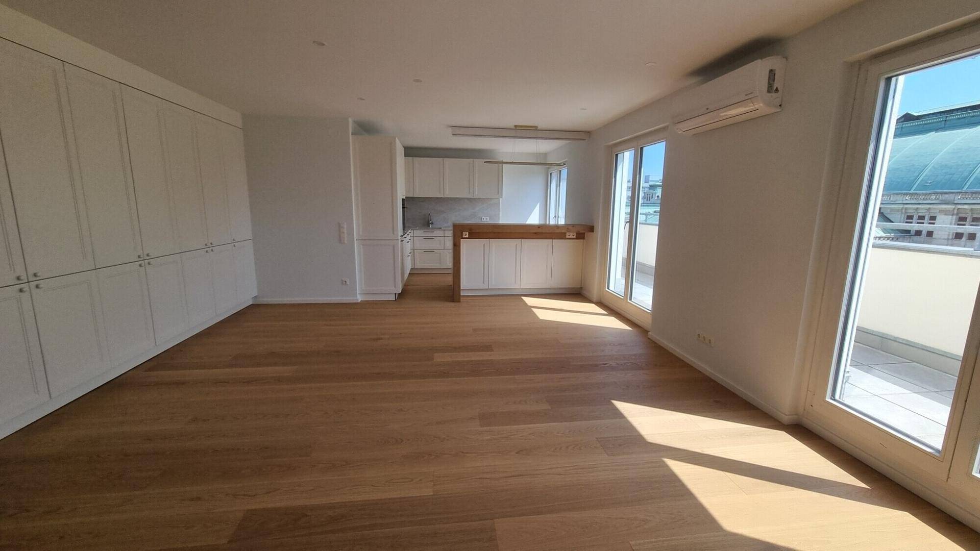 Heller Wohnbereich mit offener Küche, Holzboden und großen Fenstern mit viel Tageslicht.