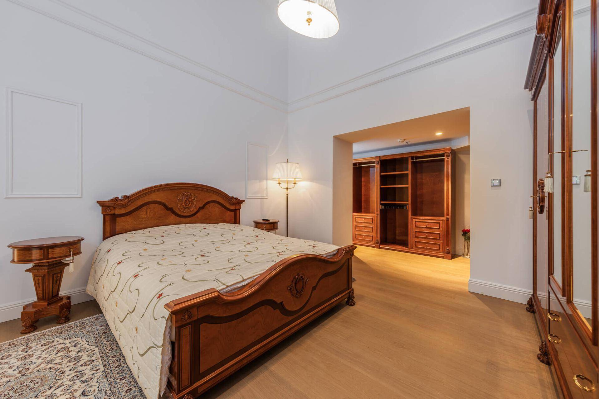 Geräumiges Schlafzimmer mit klassischem Holzbett, Parkettboden und offenem Ankleidebereich.