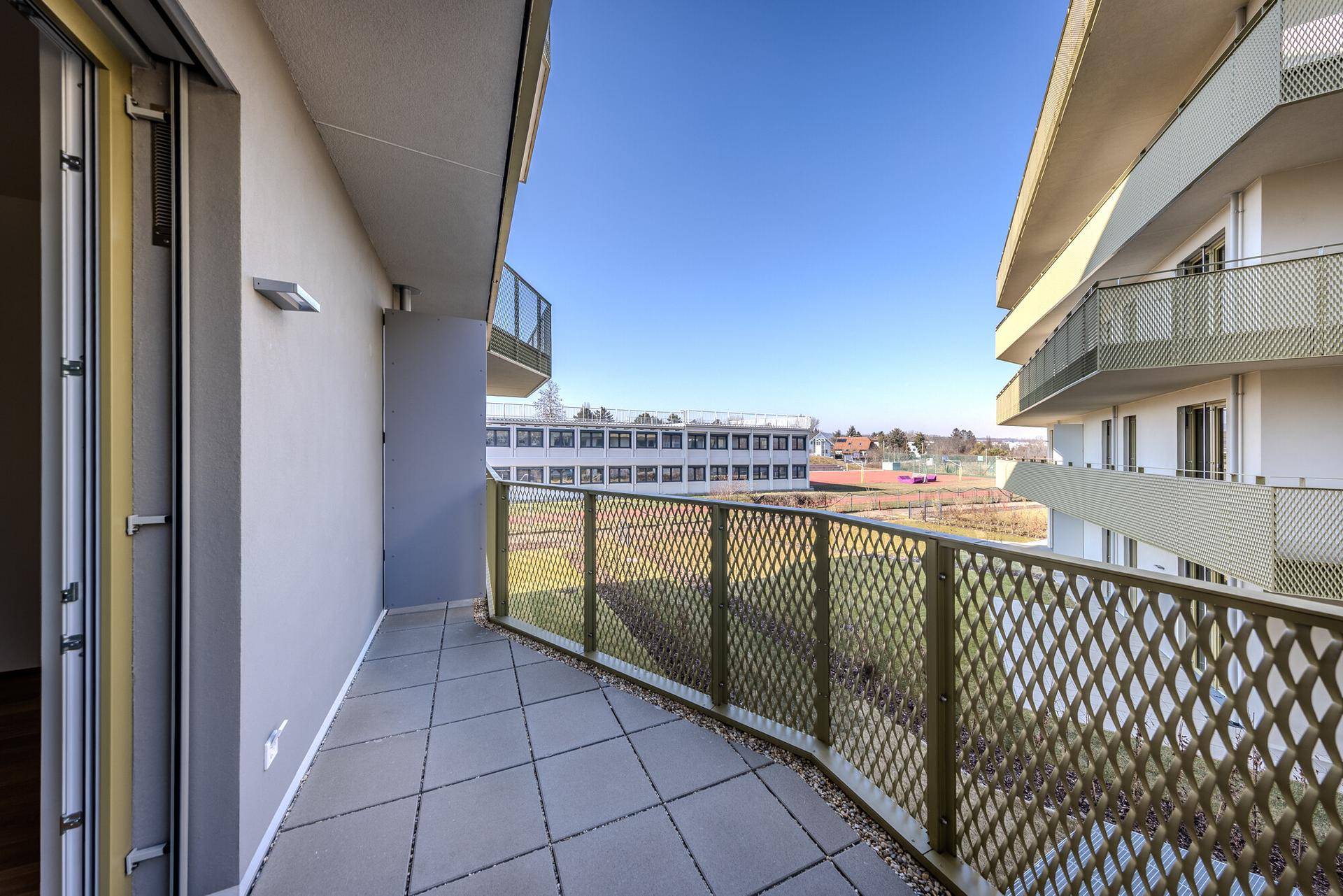 Geräumiger Balkon mit Fliesenboden und Blick auf die umliegenden Gebäude und den Himmel.