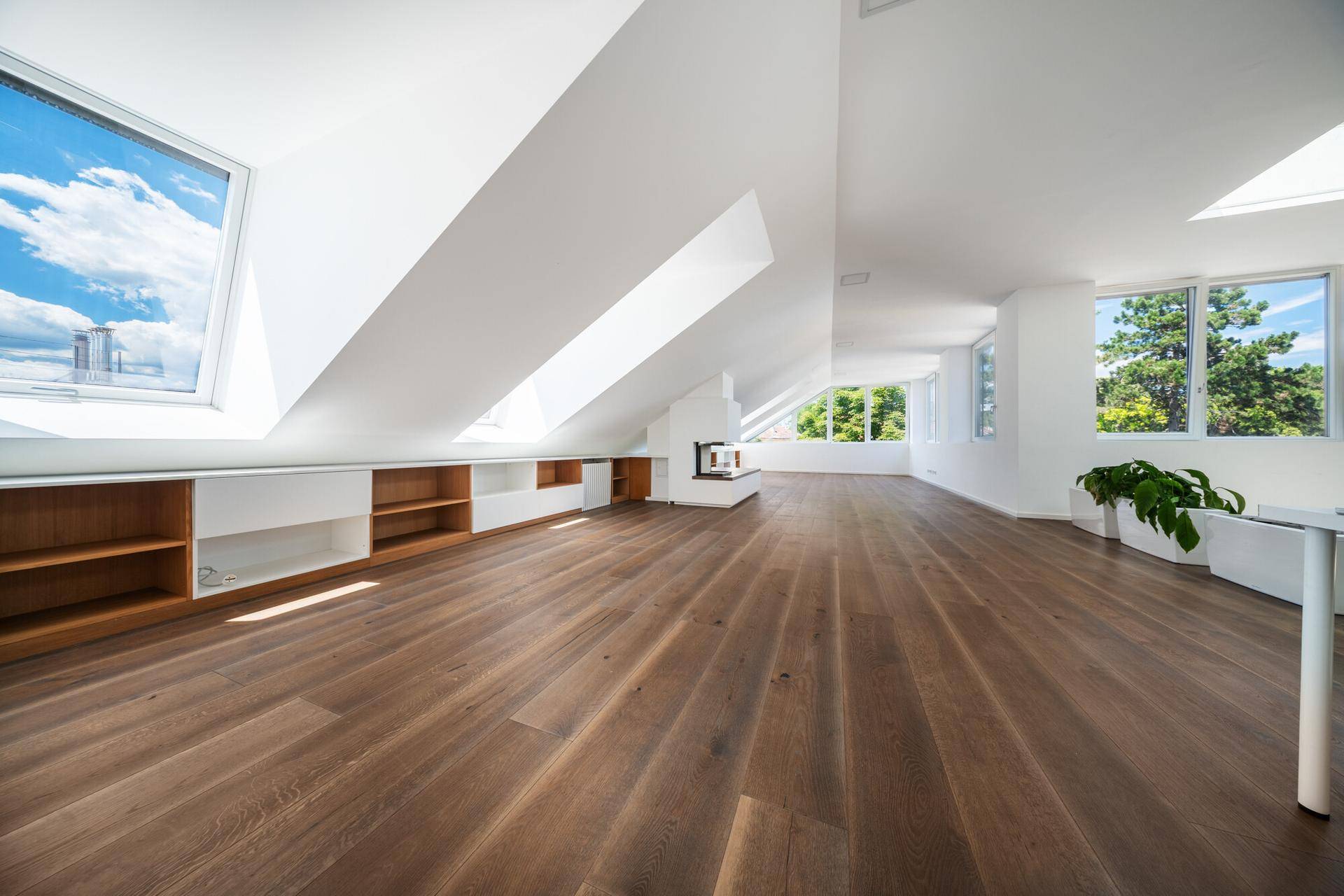 Geräumiger Dachbodenraum mit Holzdielenboden, schrägen Decken, Dachfenstern und einem modernen Kamin.