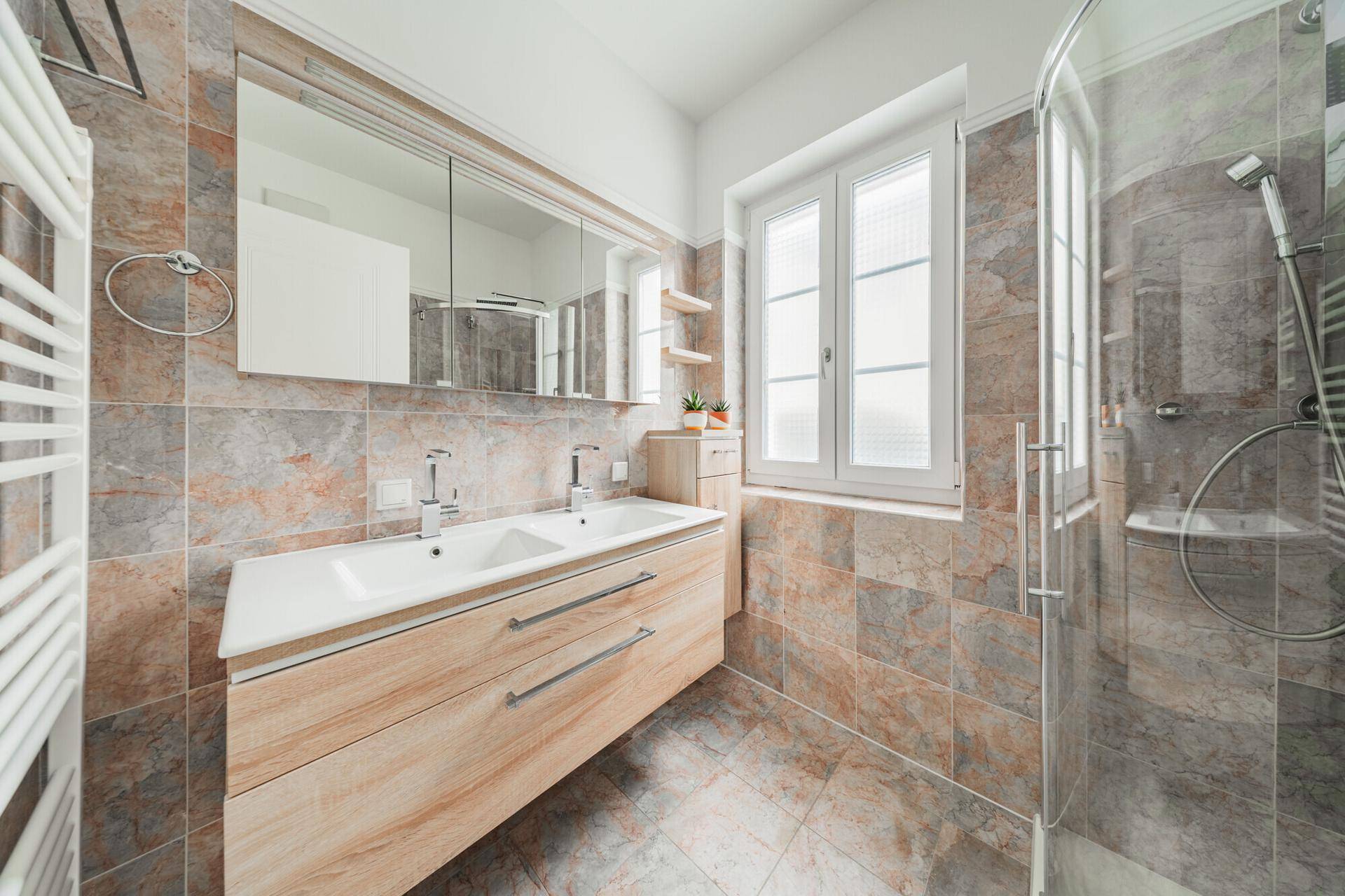 Modernes Badezimmer mit Doppelwaschbecken, großer Dusche und beheiztem Handtuchhalter.
