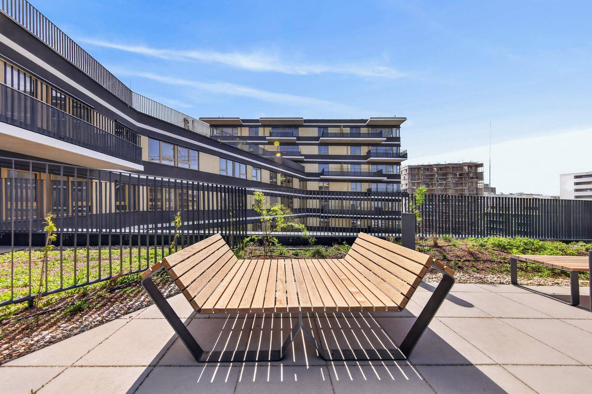 Moderne Wohnanlage mit innovativer Architektur und Sitzgelegenheiten im Außenbereich unter blauem Himmel.